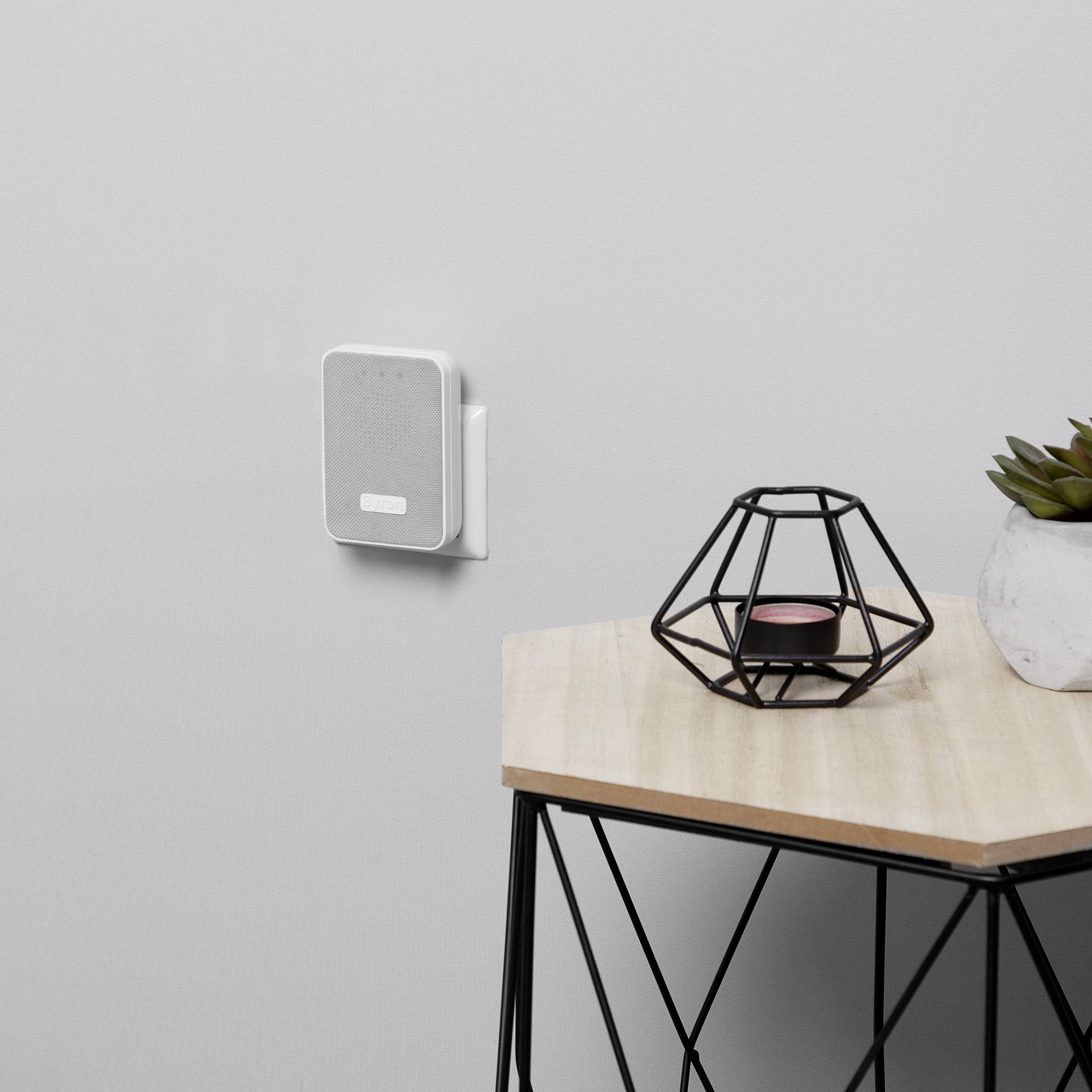 Egy WLAN-router van a falra szerelve. Mellette egy asztal áll egy geometriai formájú gyertyatartóval és egy kis zöld növénnyel.