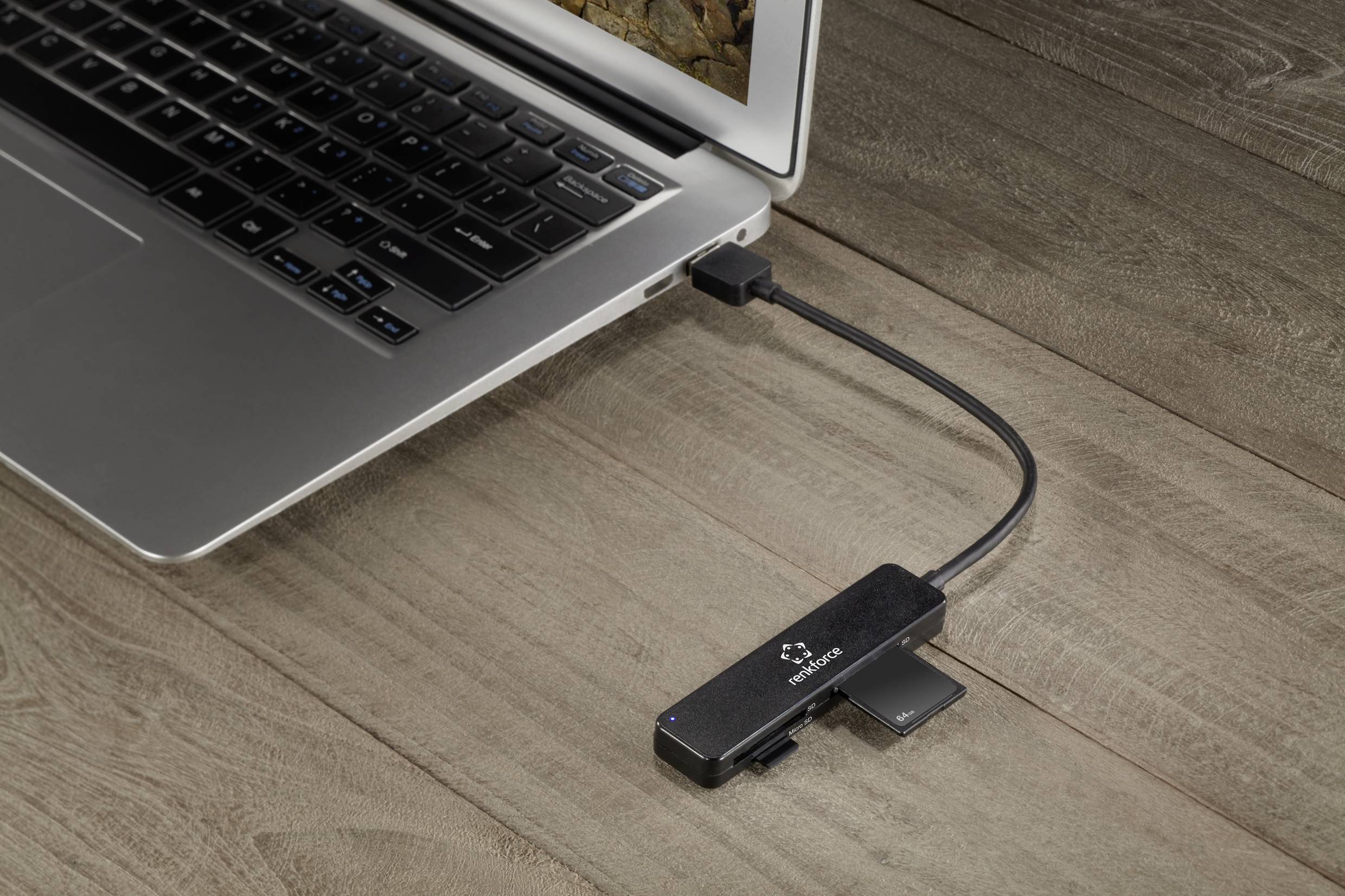 Egy pendrive USB-kábellel csatlakozik egy laptophoz, amely egy fa asztalon áll.