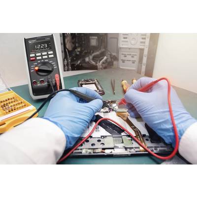 Egy személy egy multiméterrel elektronikai eszközt javít. Csavarhúzó és áramköri lap látható az asztalon.