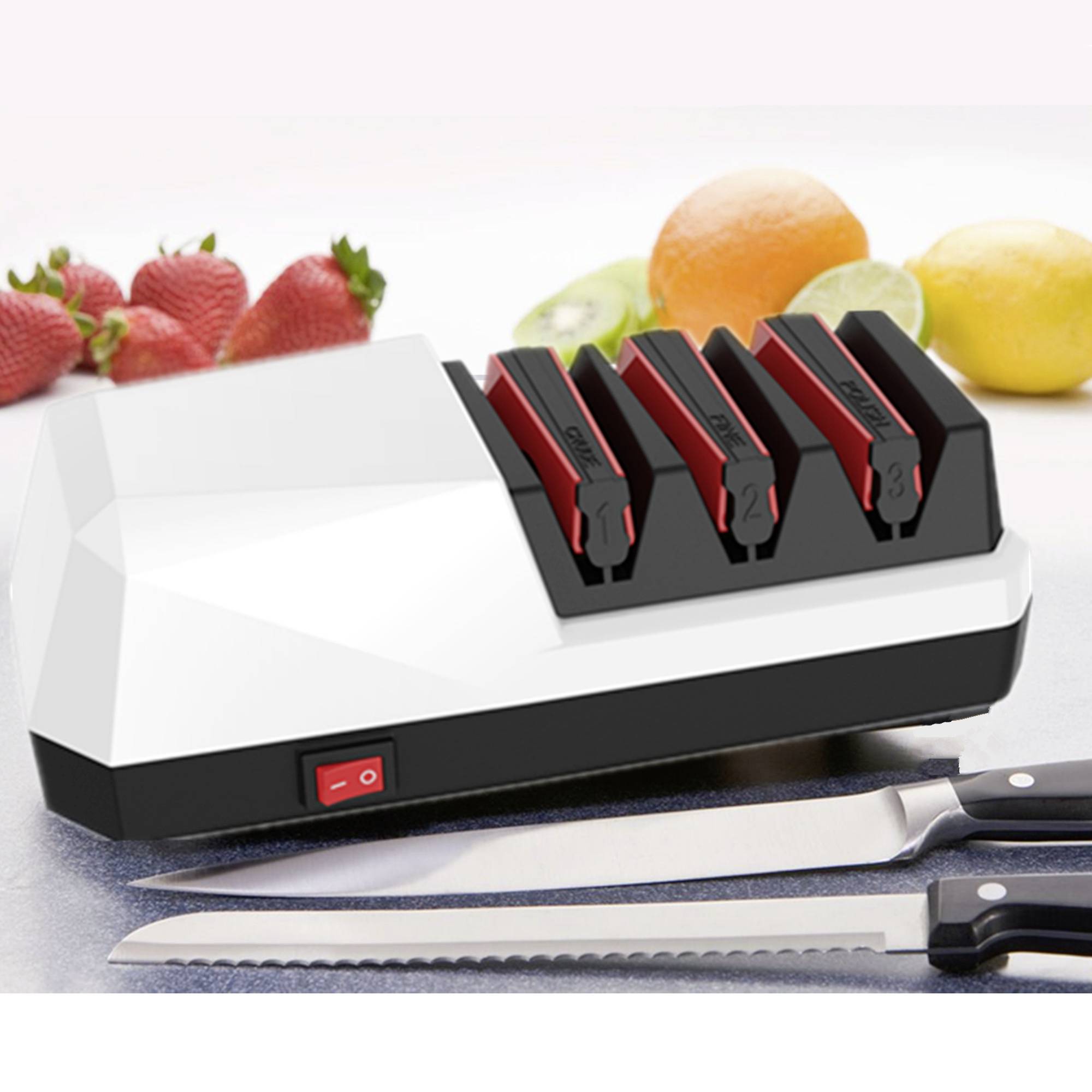 Egy háromfokozatú elektromos késélező, amely friss gyümölcsök és két konyhai kés társaságában egy munkafelületen helyezkedik el.