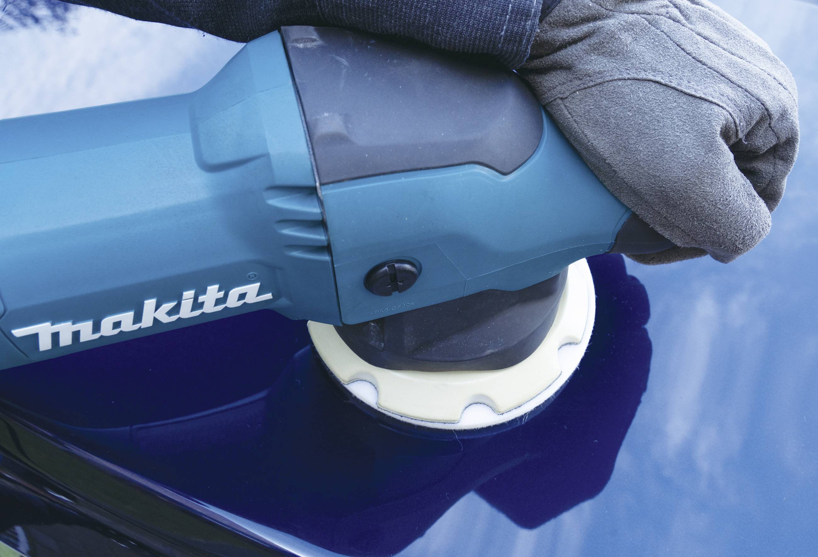 Egy kesztyűs kéz egy Makita polírozógépet tart, miközben egy kék felületet políroznak.