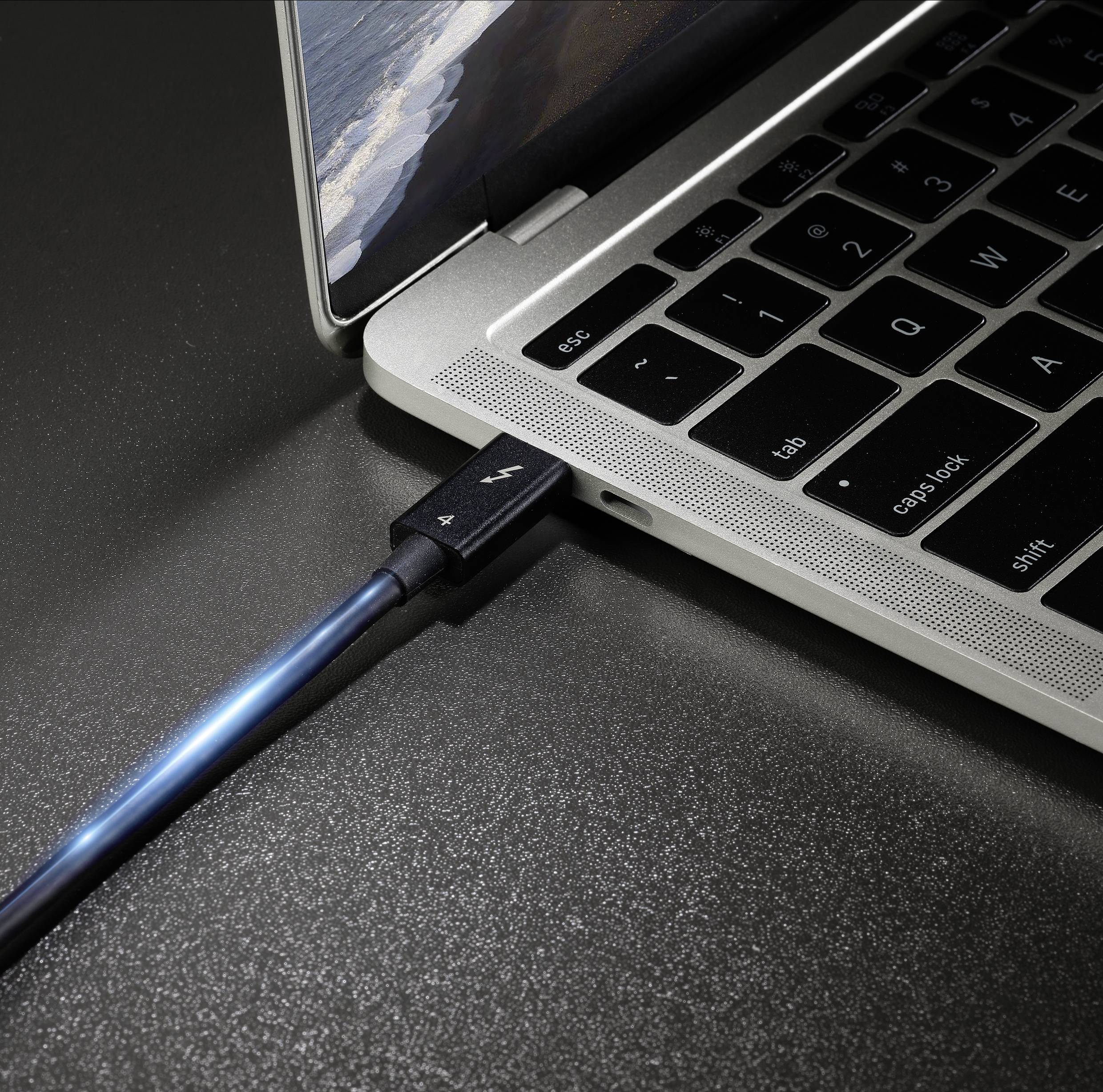 Egy kék USB-kábel csatlakoztatva van egy laptophoz. A laptop képernyőjének és billentyűzetének egy részlete látható közeli felvételben.