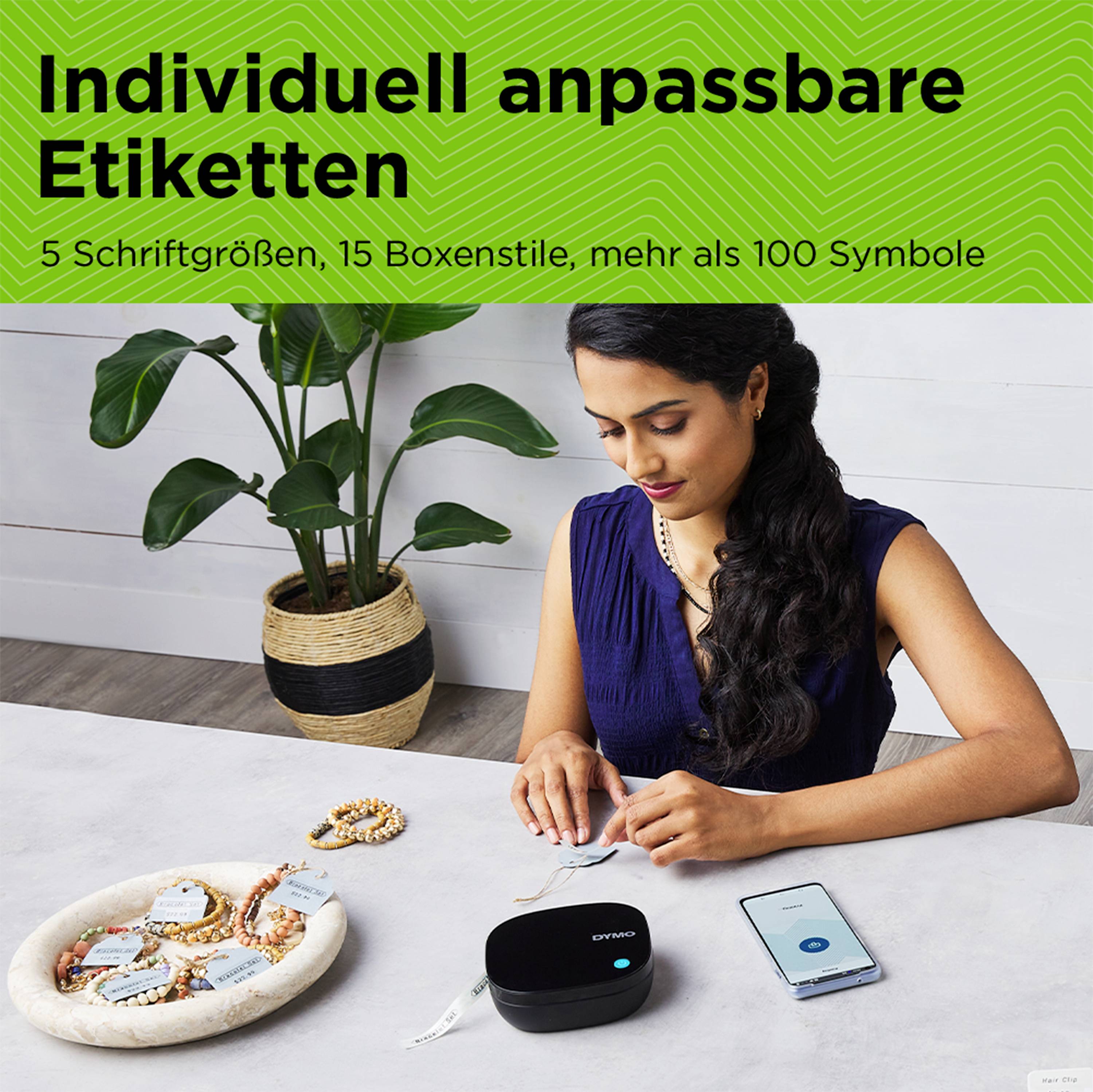 Egy nő ül az asztalnál, és egy okostelefon-applikációval vezérelt modern nyomtatót használ címkék készítéséhez. Szöveg: 'Egyedileg testre szabható címkék'.