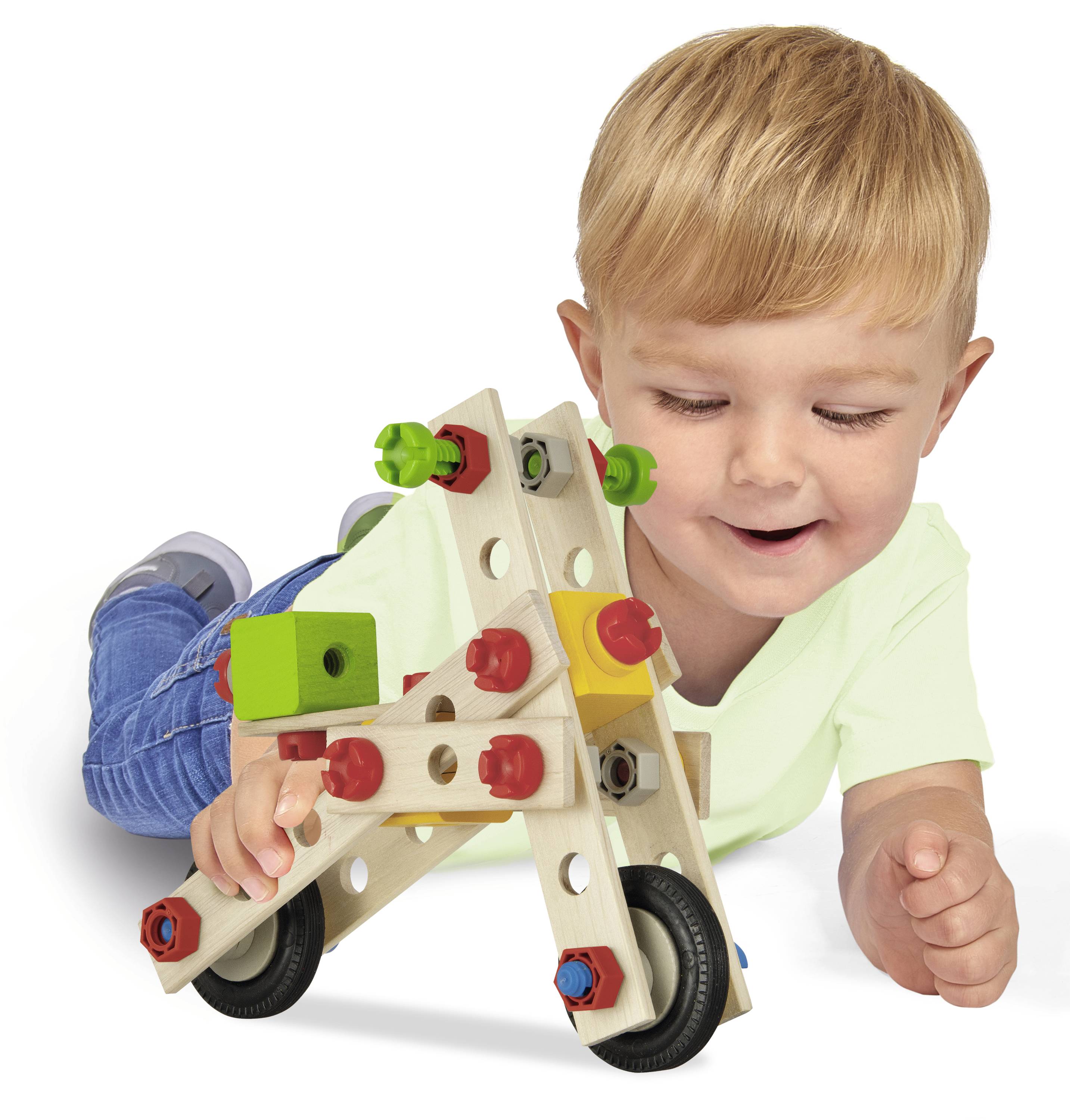 Egy gyerek vidáman játszik egy fa építőjátékkal a padlón, amely színes elemeket és kerekeket tartalmaz.