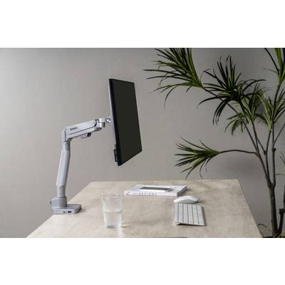 Egy modern íróasztal számítógépes monitorkarral, billentyűzettel, egy pohár vízzel és egy növénnyel a háttérben.