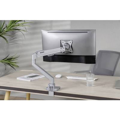 Egy íróasztal egy állítható karú számítógépes monitorral, billentyűzettel és egy pohár vízzel rajta; a háttérben szürke fal és egy növény.