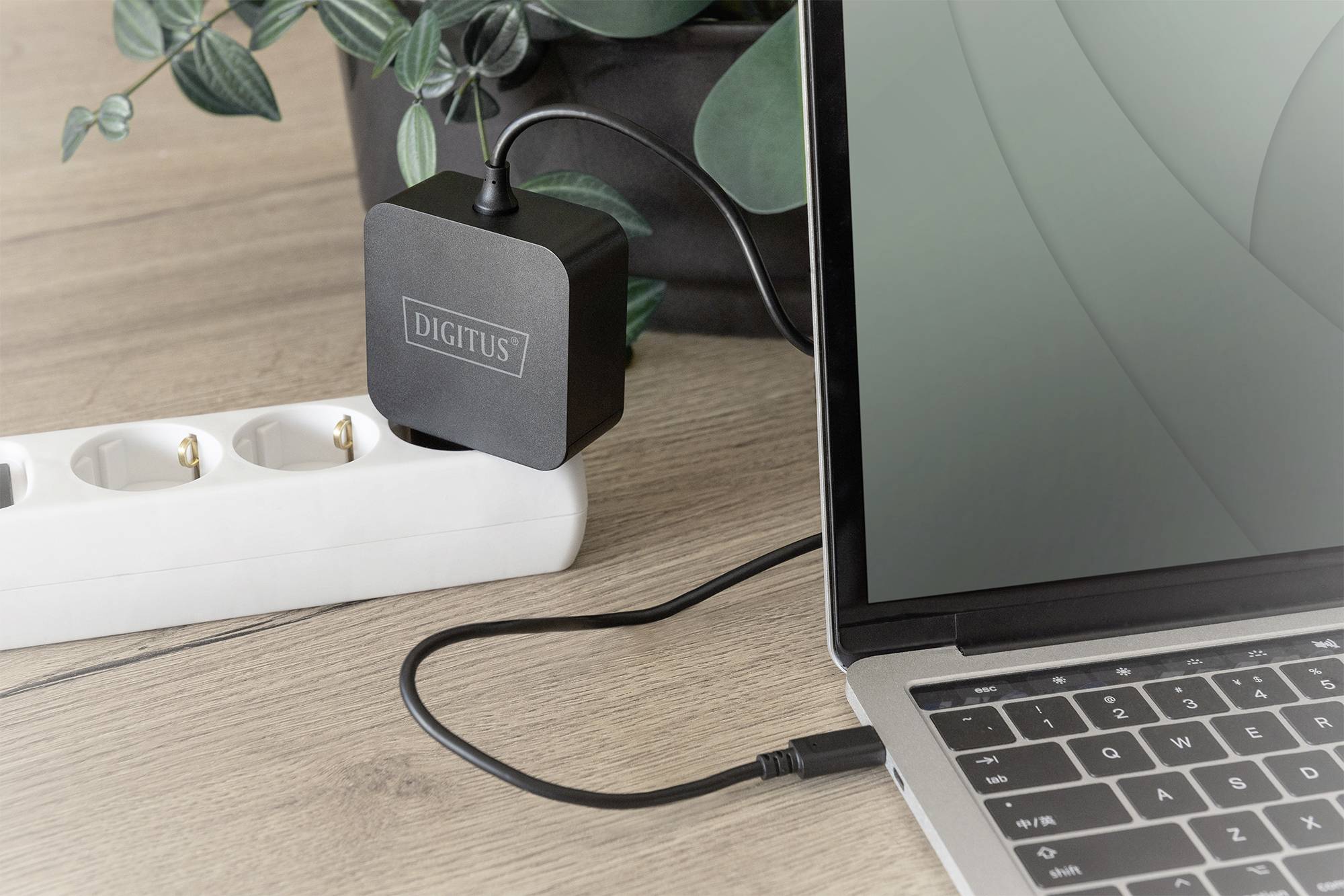 A kép egy laptopot mutat, amely egy hálózati adapterhez csatlakoztatva van. Az adapter egy elosztóban van bedugva.