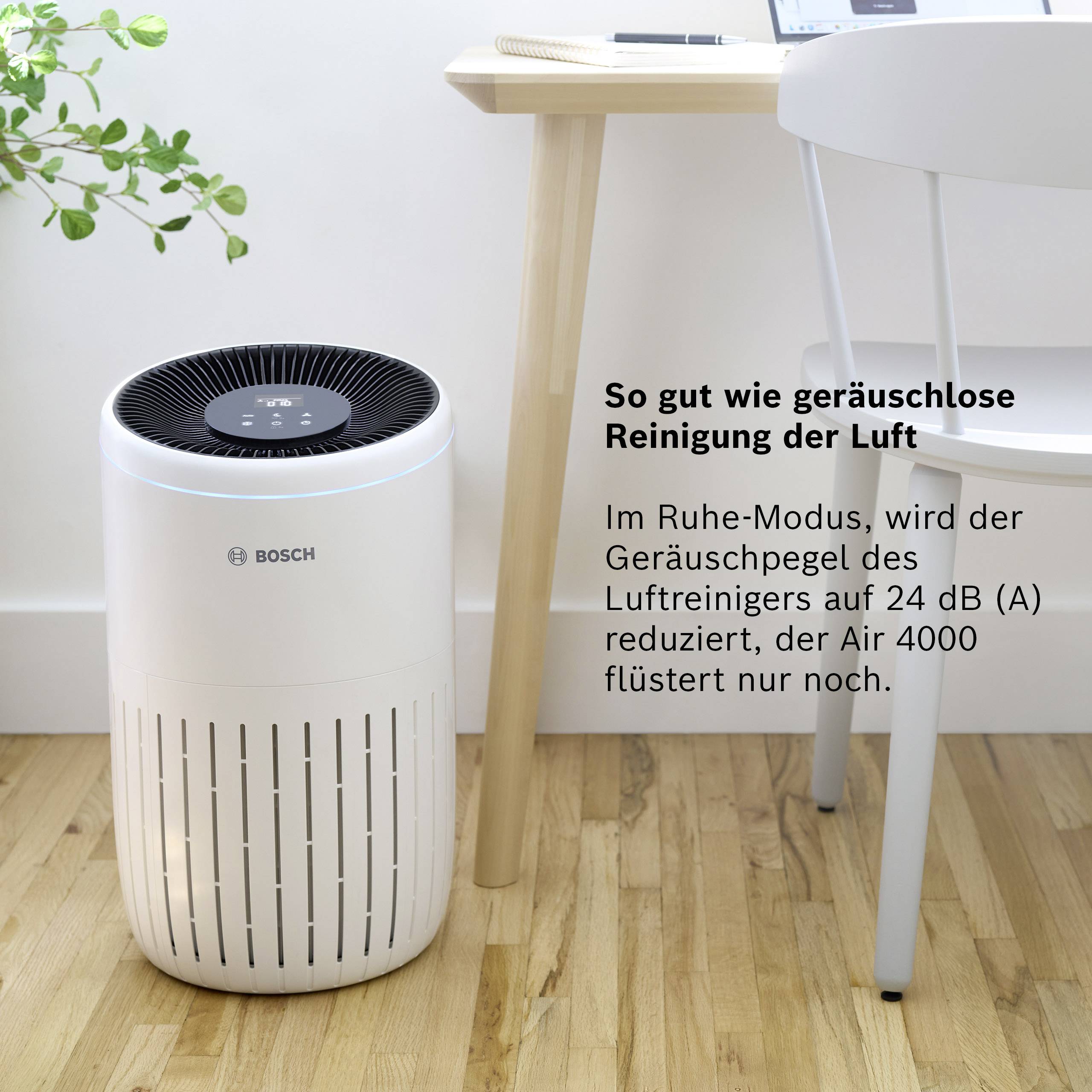 Egy légtisztító egy fapadlón áll egy asztal és egy szék mellett. Szöveg a képen: 'Szinte zajmentes levegőtisztítás'.