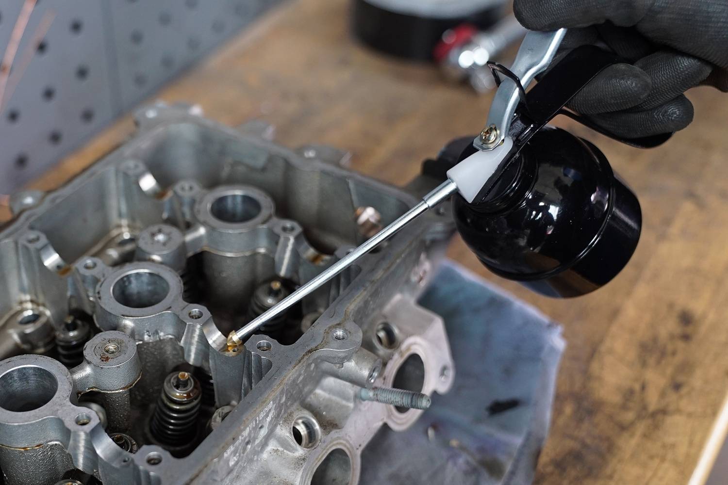 Egy személy egy motorblokk tisztítását végzi egy olajpermetező készülékkel egy munkapadon egy műhelyben.