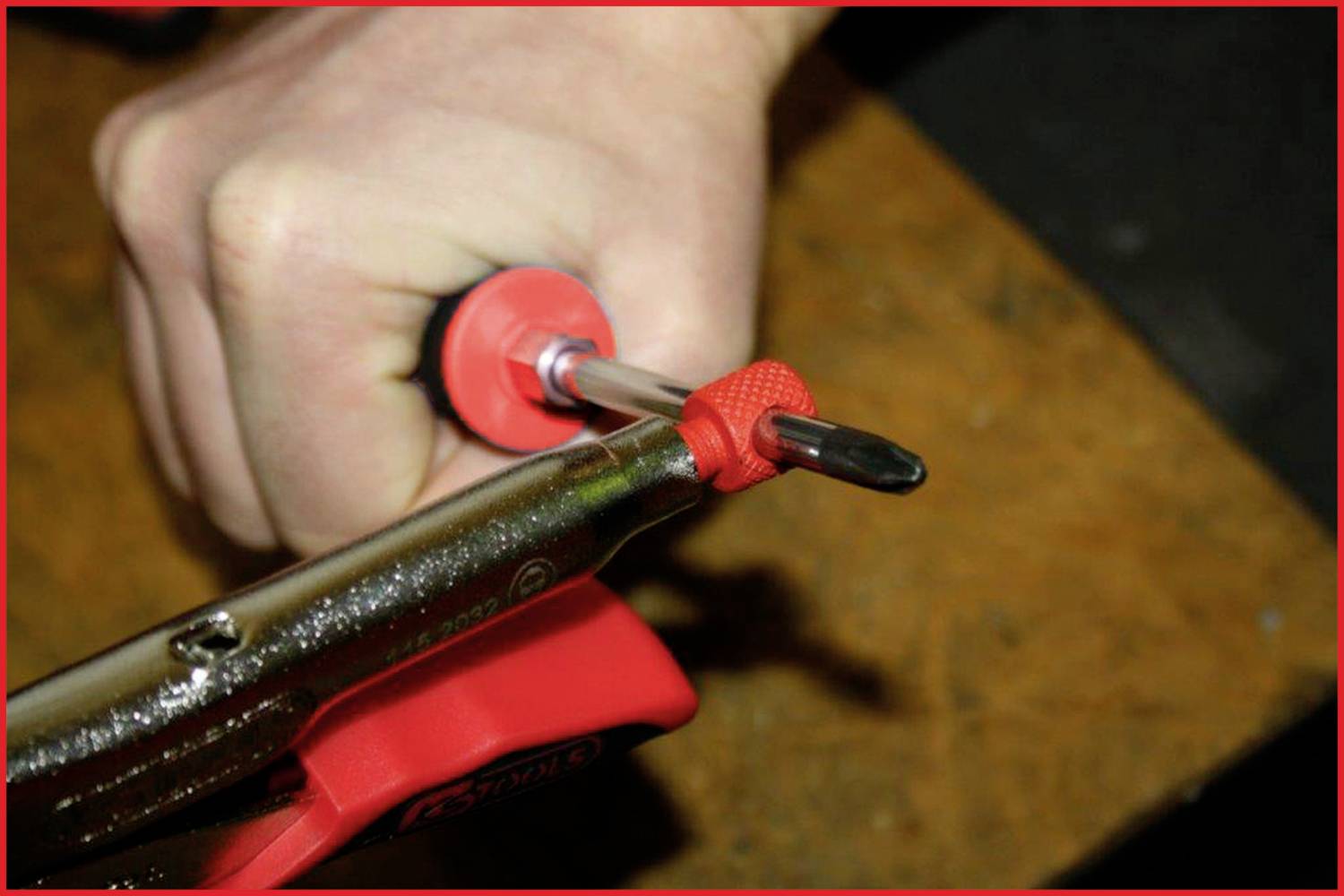 Egy kéz egy csavarhúzót tart, amely egy piros satuba van befogva.