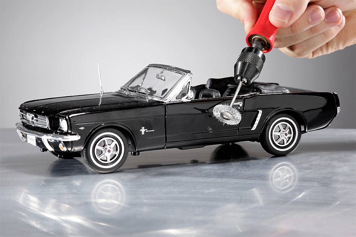 Egy fekete Ford Mustang kabrió modellautót egy piros fúrógép munkál meg, amelynek kis csiszolófeltéte van.