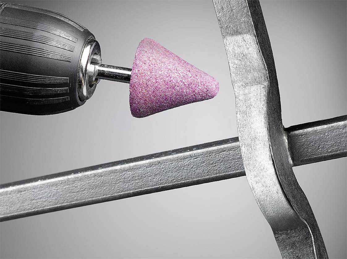 Egy közelkép egy rózsaszín csiszolófejű forgácsolószerszámról, amint egy fémszélen dolgozik.