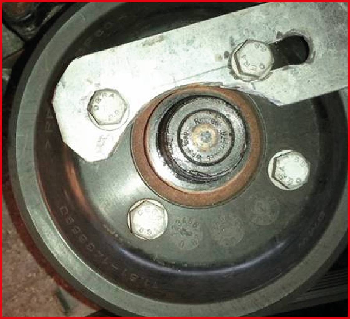 Egy fémből készült fogaskerék- vagy szíjrendszer közeli felvétele csavarokkal és központi tengellyel, valószínűleg egy motor alkatrésze.