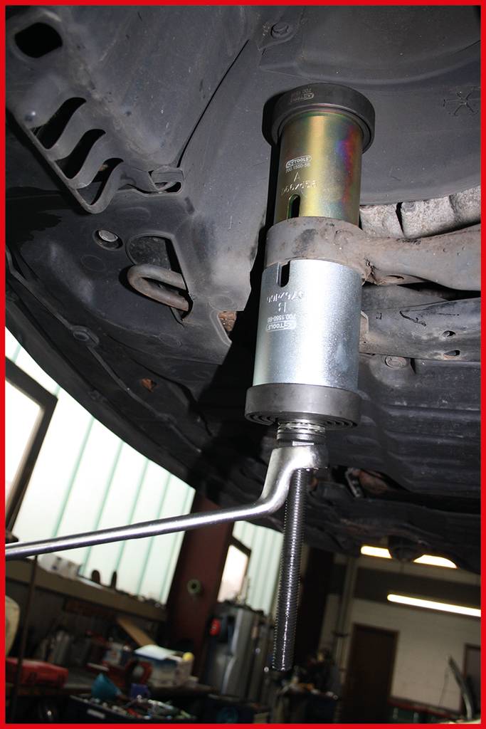 Egy rugófeszítő szerszámot használnak egy autó rugóinak feszítéséhez. A jelenet egy autószerelő műhelyben játszódik.