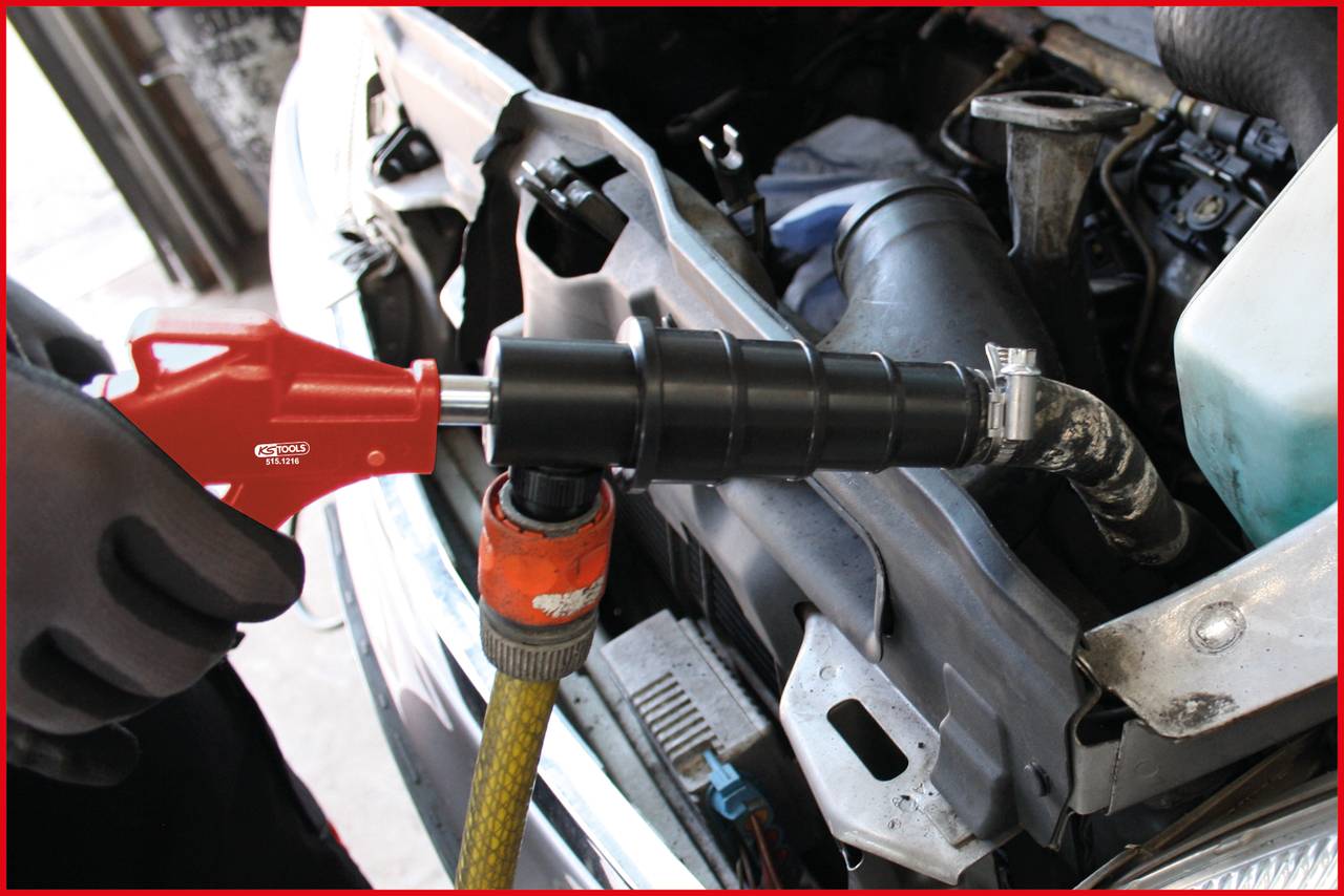 Egy fekete fúvókával ellátott tömlőt csatlakoztatnak egy jármű hűtőrendszeréhez. Egy piros kar látható.