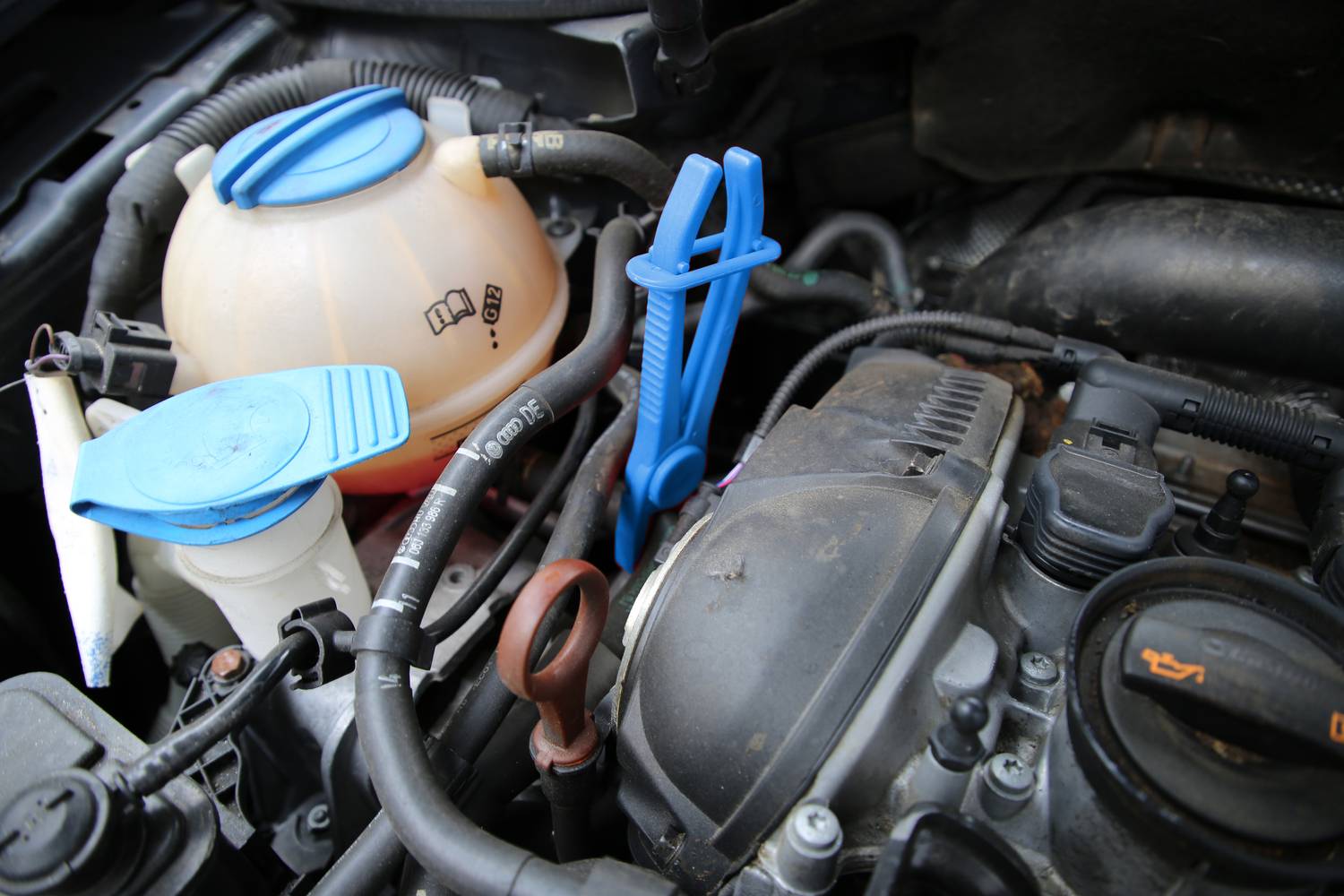 Autószerelő műhely: Pillantás egy motortérre, nyitott hűtőfolyadék-tartállyal, műanyag rögzítővel és csövekkel.