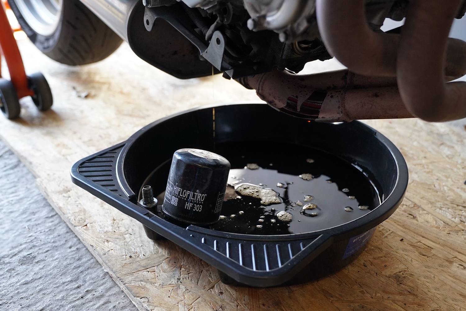 Egy gépjármű olajleeresztési folyamata. Olaj csepeg a motorból egy gyűjtőedénybe. Egy használt olajszűrő fekszik mellette.