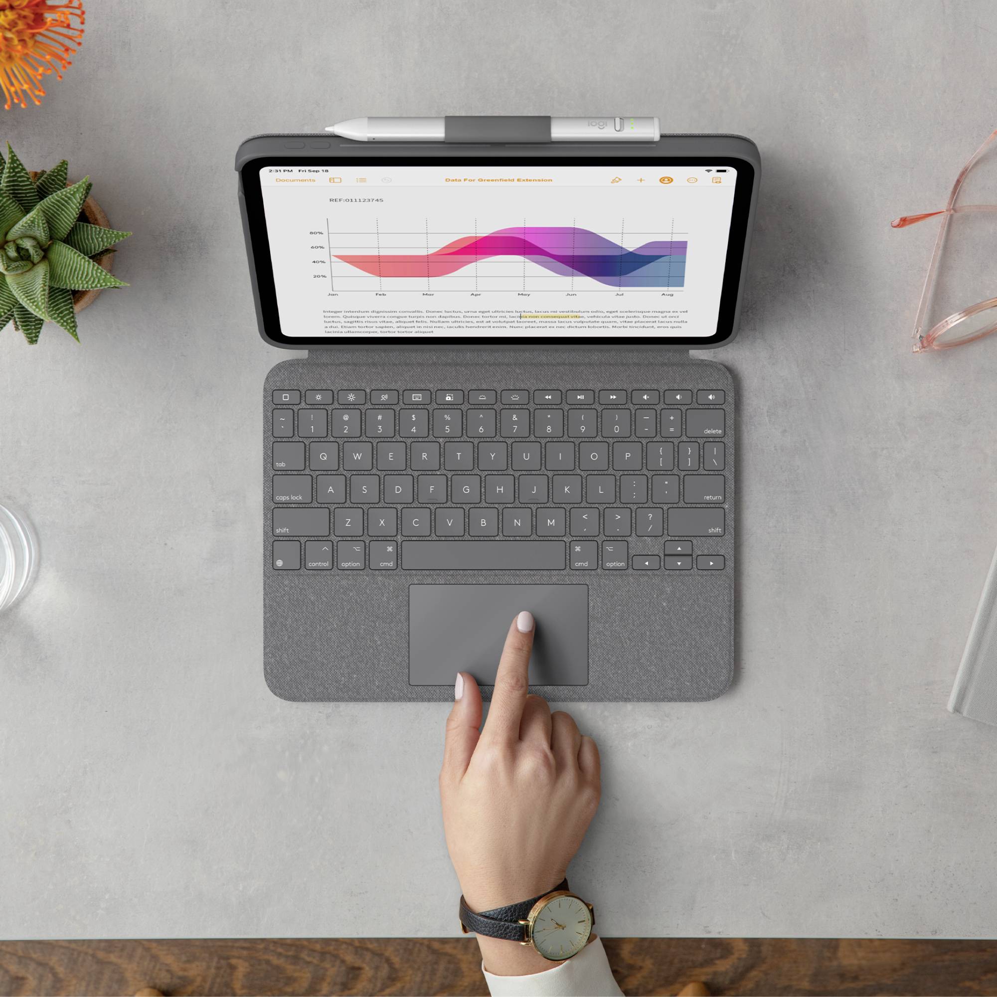 Egy tablet egy diagramot mutat emelkedő és csökkenő értékekkel. Egy kéz érinti a trackpadot egy billentyűzeten a tablet előtt.