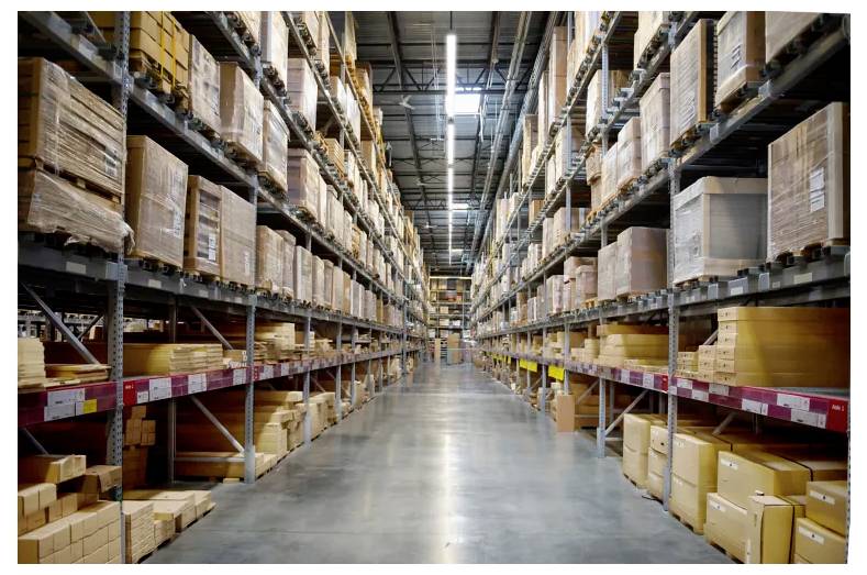 Nagy raktár folyosója, amely mindkét oldalán magas rakodópolcokkal szegélyezett, amelyekre dobozos készleteket raktak fel.