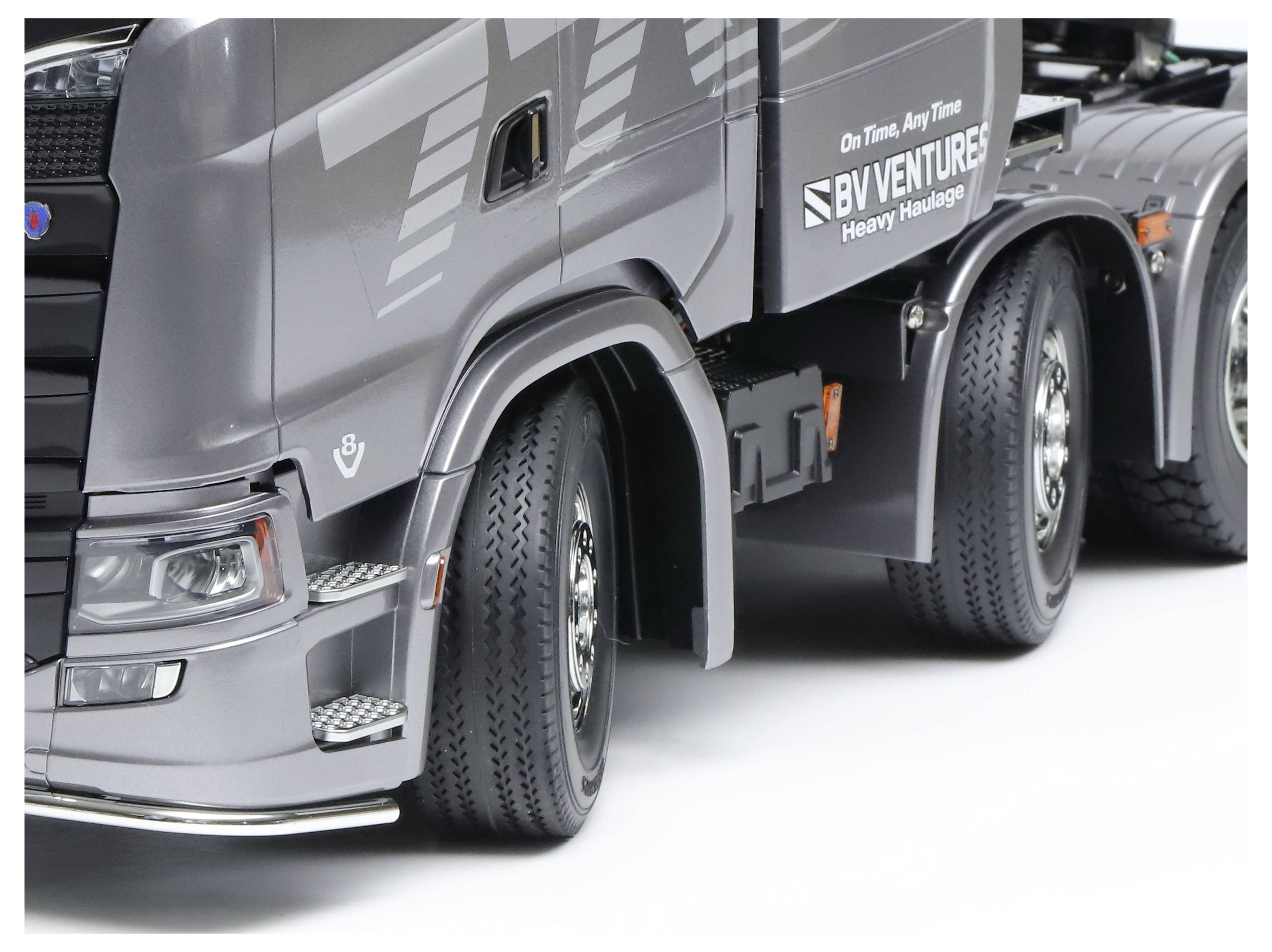 Szürke teherautó a 'BV VENTURES Heavy Haulage' felirattal az oldalán, fehér háttér előtt áll mozdulatlanul.