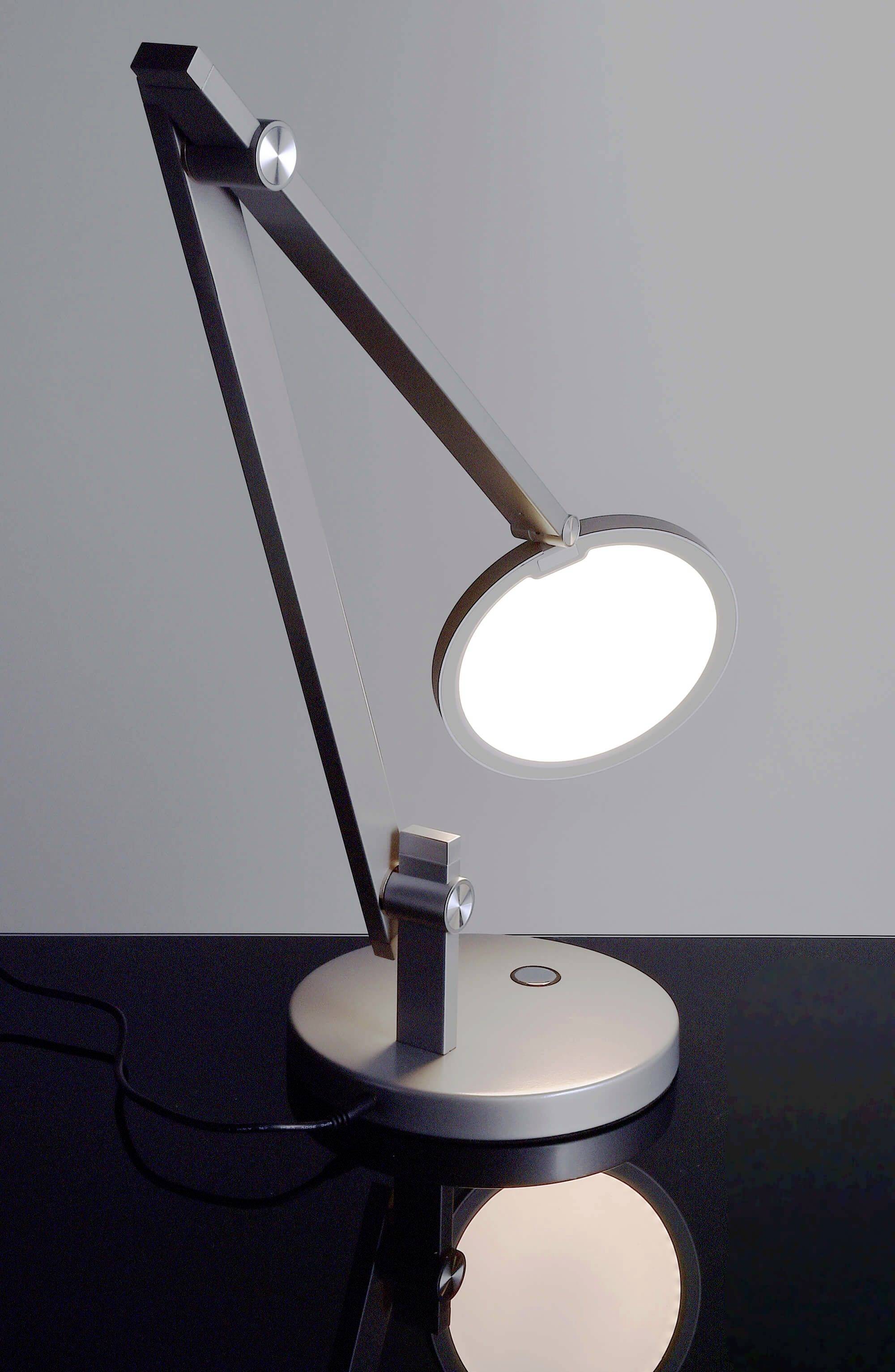 Modern asztali lámpa állítható karral és kerek, világító ernyővel, sötét asztalon elhelyezve, minimalista stílusban.