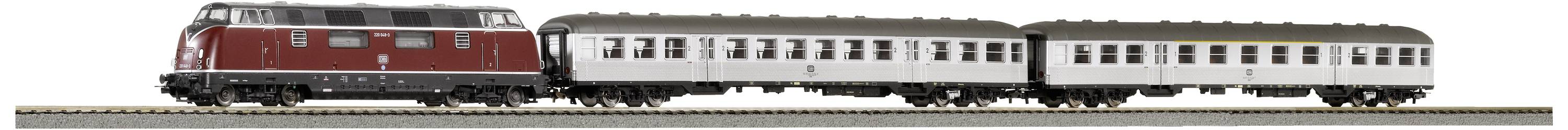 Egy piros mozdony két fehér utaskocsival egy sínpályán halad.