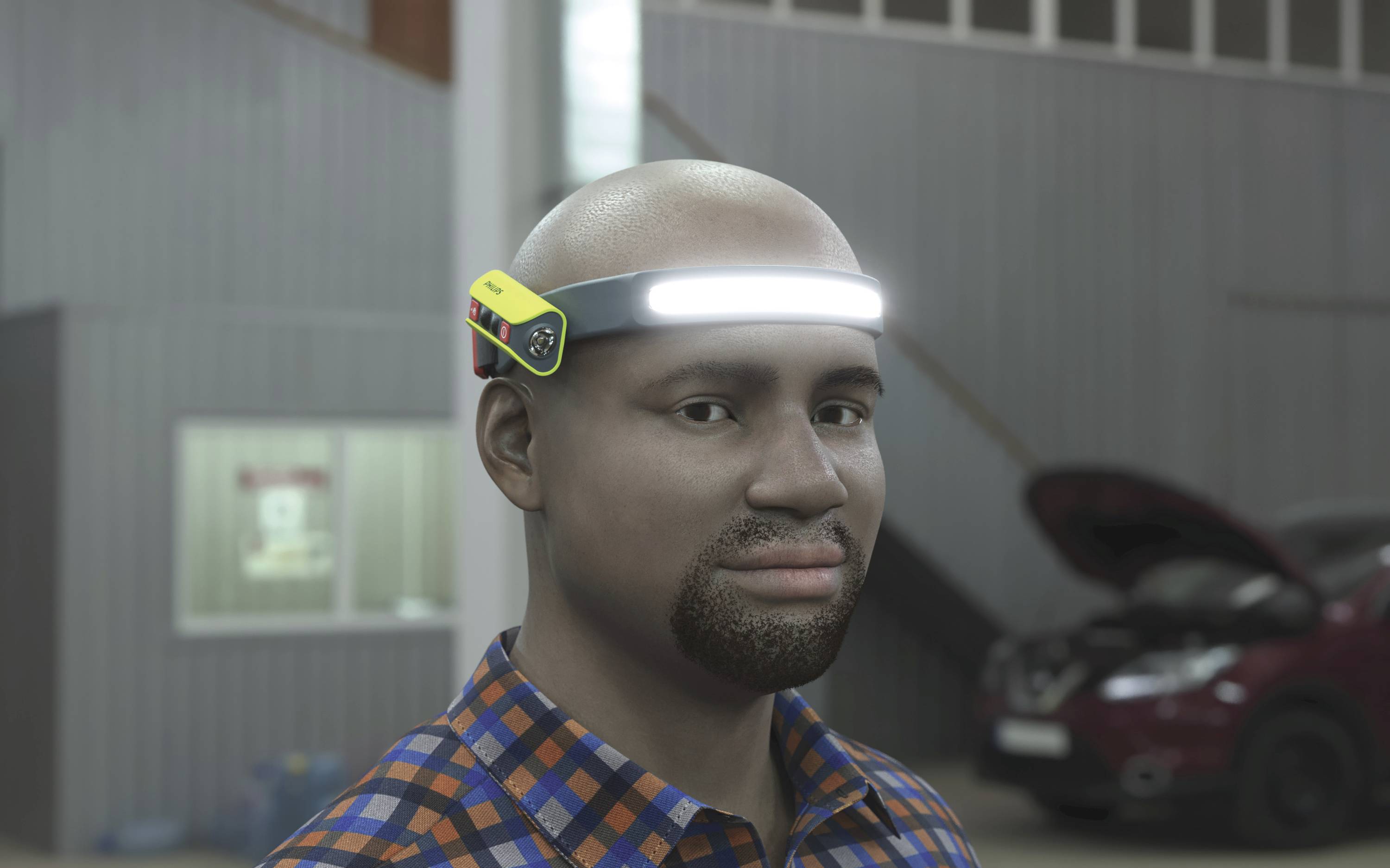 Egy mosolygó férfi LED-es fejpántot visel egy műhelyben. A háttérben egy autó áll nyitott motorháztető mellett.