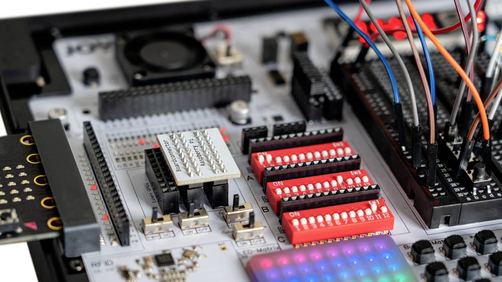 Egy elektronikai áramkör közeli felvétele, amelyen több chip, csatlakozók és színes kábelek láthatók. Fejlesztői modul egy technikai környezetben.