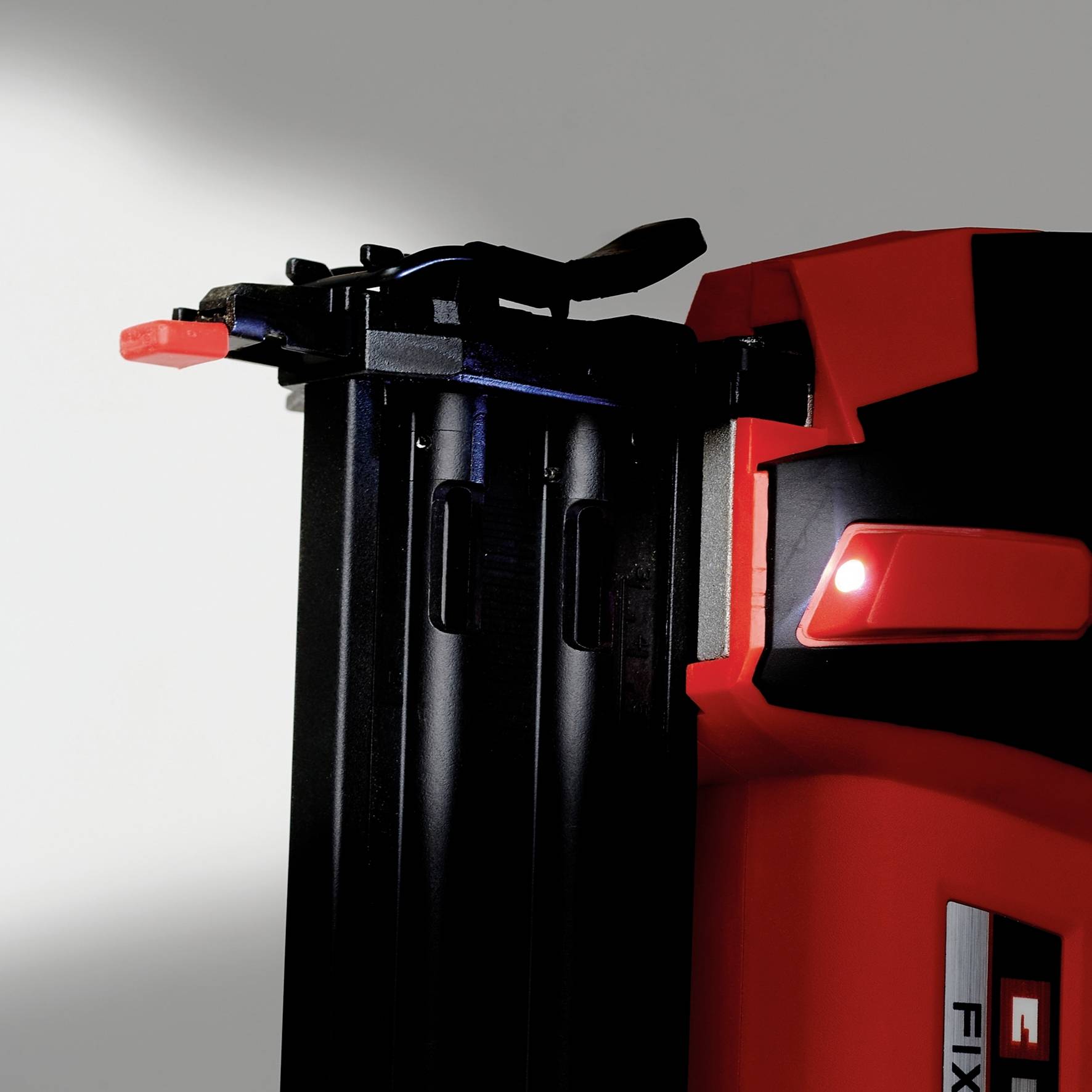 Egy piros-fekete szerszám fekete tárral és piros emelőkarral, amely egy fehér fal felé irányul.