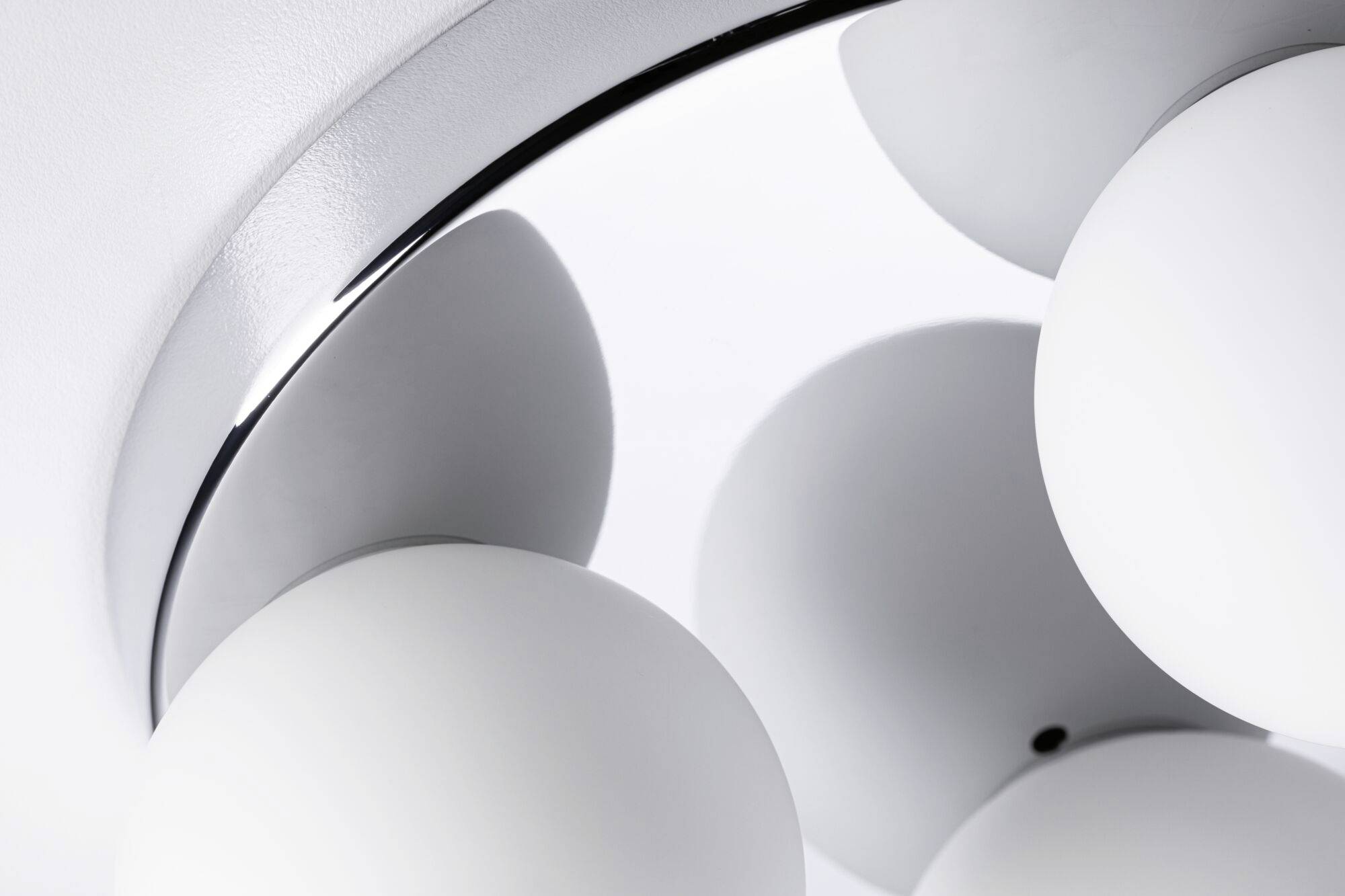 Közeli felvétel egy modern mennyezeti lámpáról, amelynek gömb alakú, fehér üvegbúrái fémtartóra vannak erősítve.