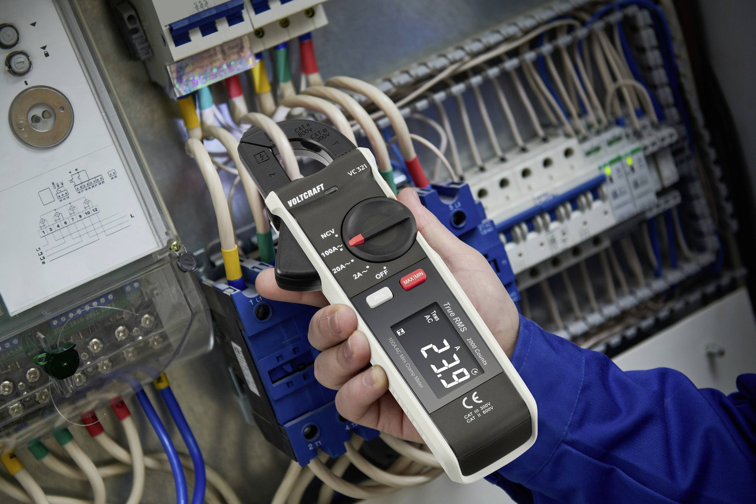 Egy személy ampermérő fogóval méri az áramfolyást egy elektromos elosztószekrényben. A kijelzőn '52,2 A' látható.