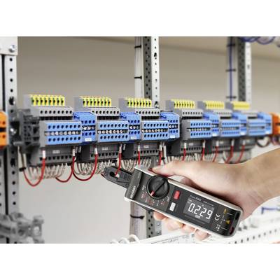 Egy kéz egy digitális mérőkészüléket tart, amely egy elosztószekrényhez csatlakozik. A kijelzőn '0.2239' érték látható mérés közben.