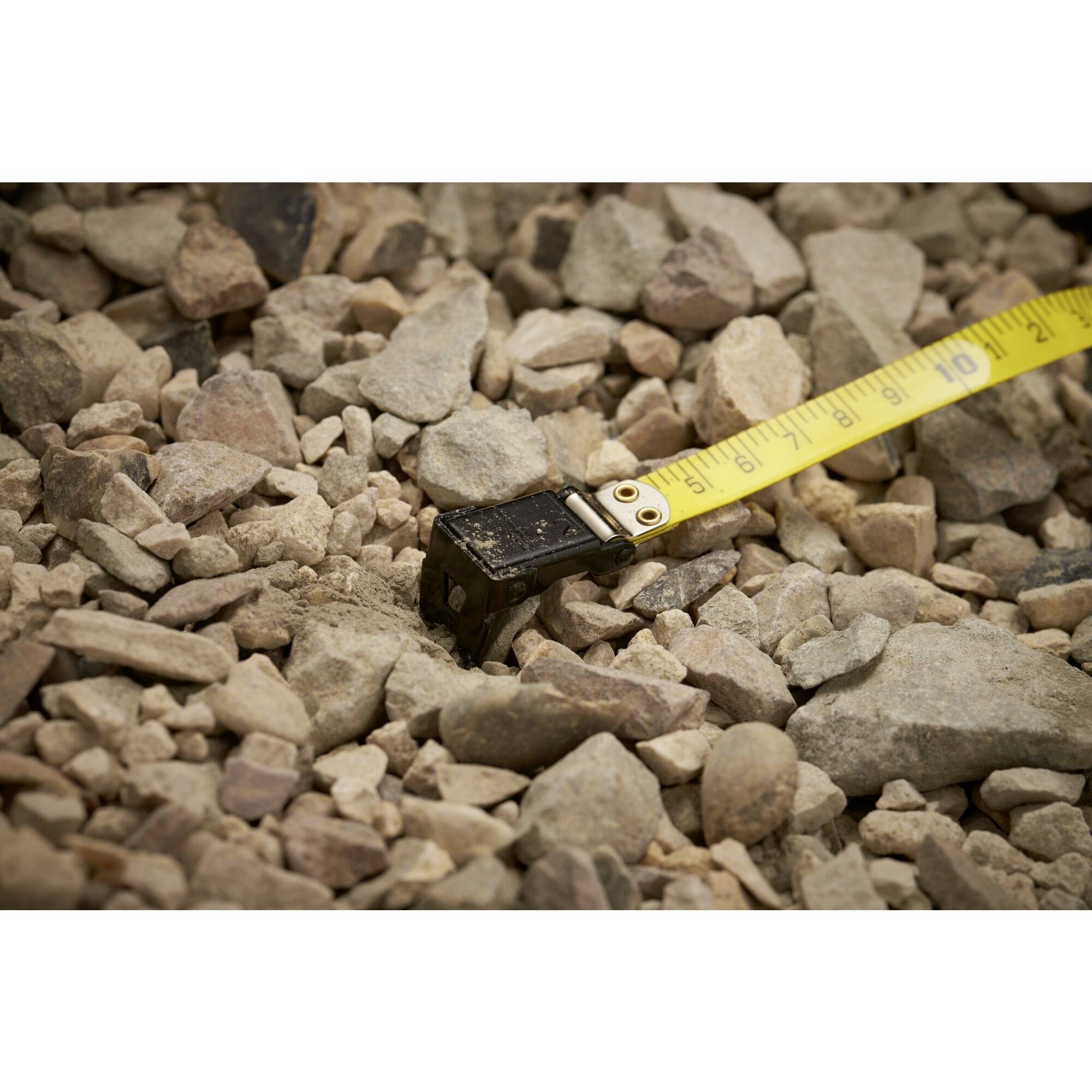 Egy mérőszalag fekszik egy kisméretű, szabálytalan alakú kövekből álló felületen, és egy mérést mutat.