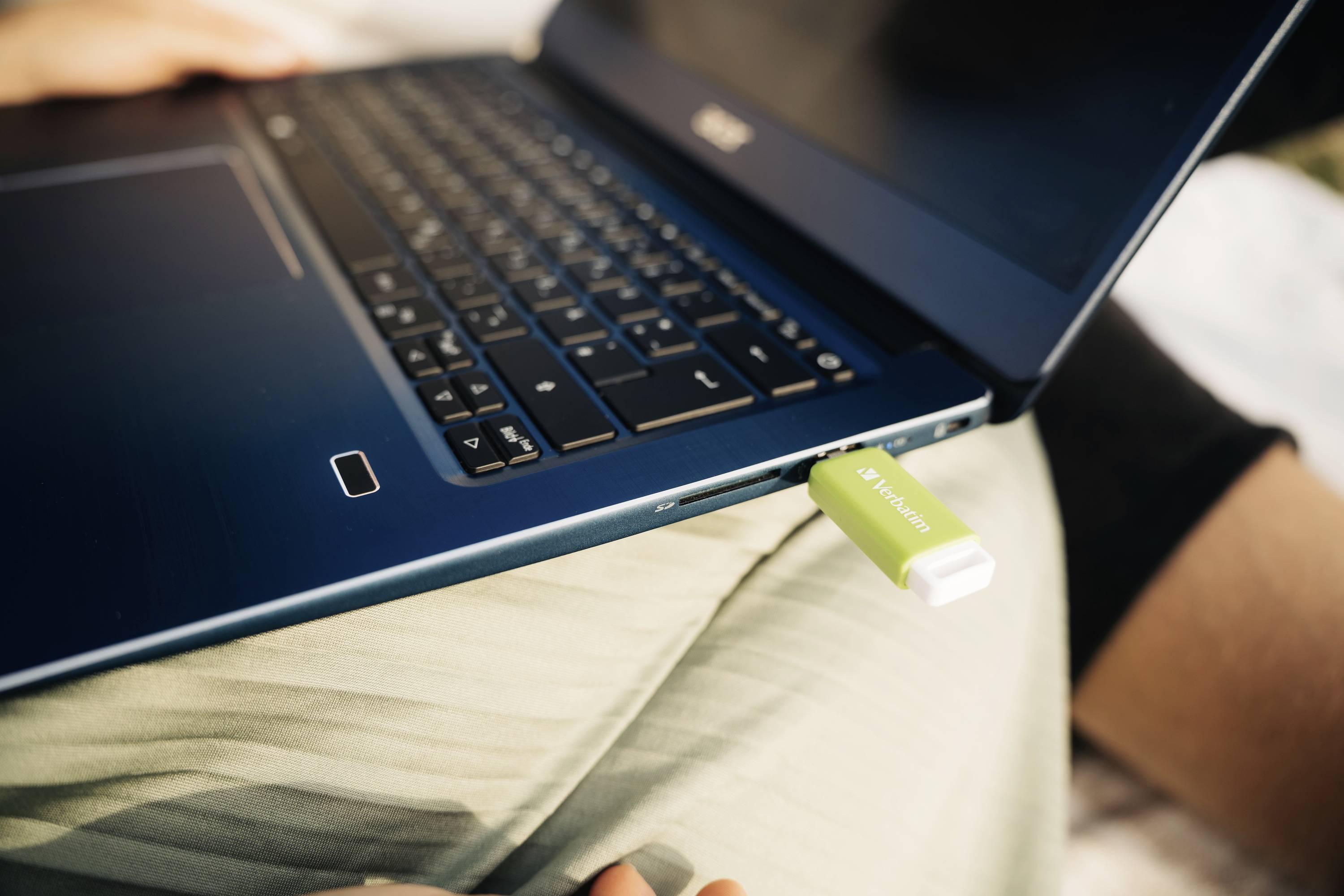 Egy zöld pendrive van bedugva egy kék laptopba, amely egy világos felületen fekszik.