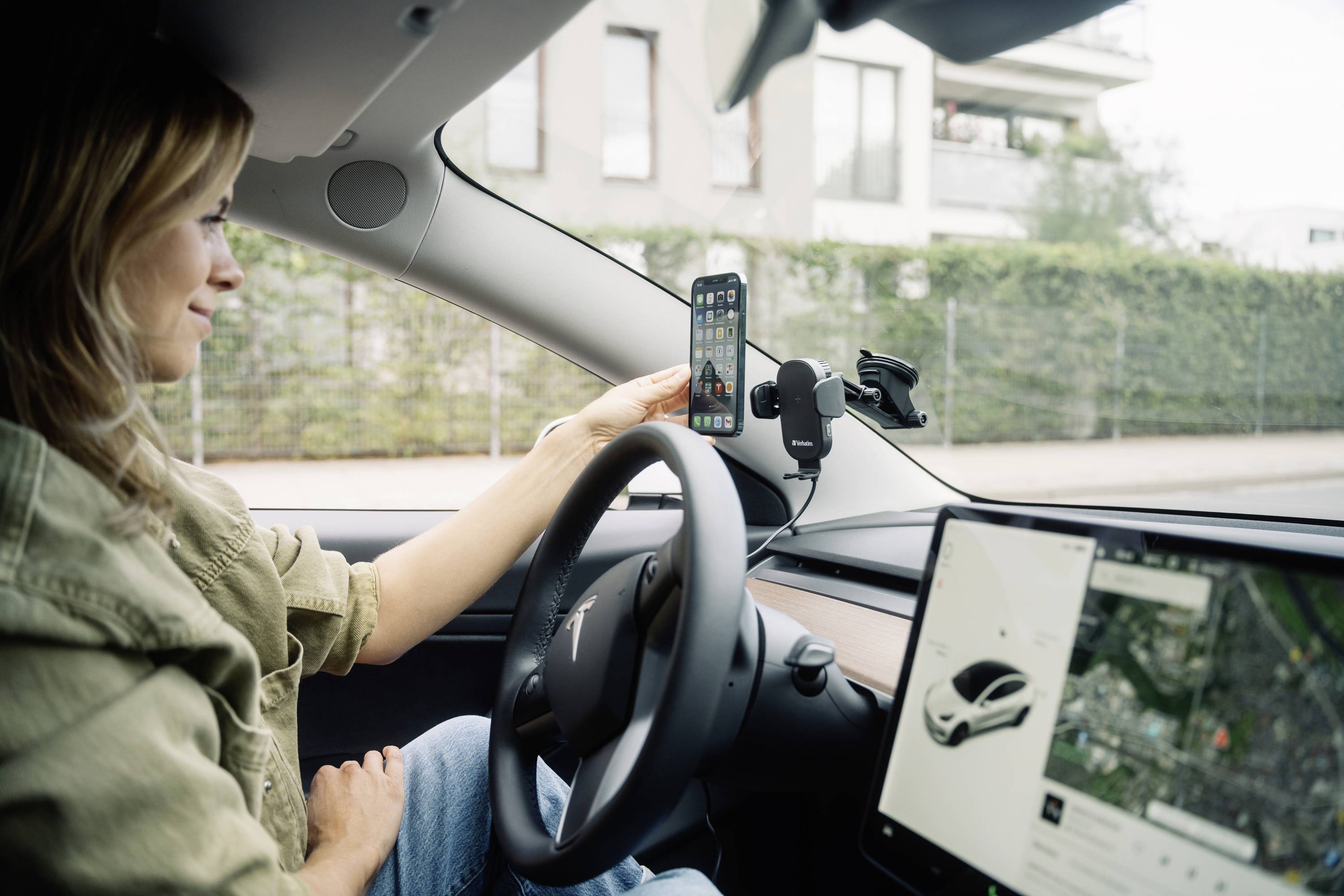 Egy személy ül egy autóban és rögzíti okostelefonját a műszerfalon lévő tartóba. Az autóban navigációs rendszer látható.