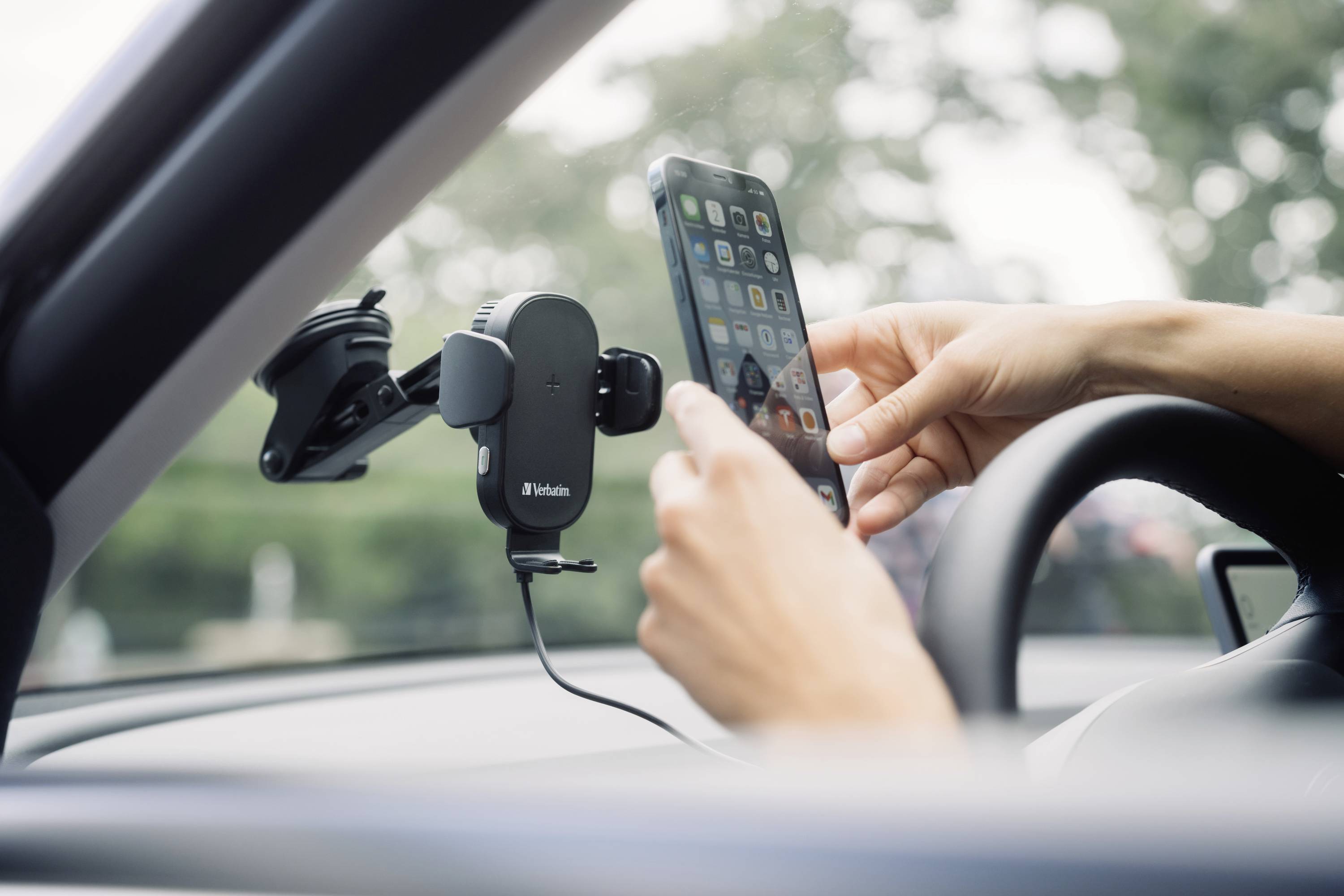 Egy személy egy mobiltelefont rögzít egy autós telefontartóban. A tartó a szélvédőre van felszerelve.