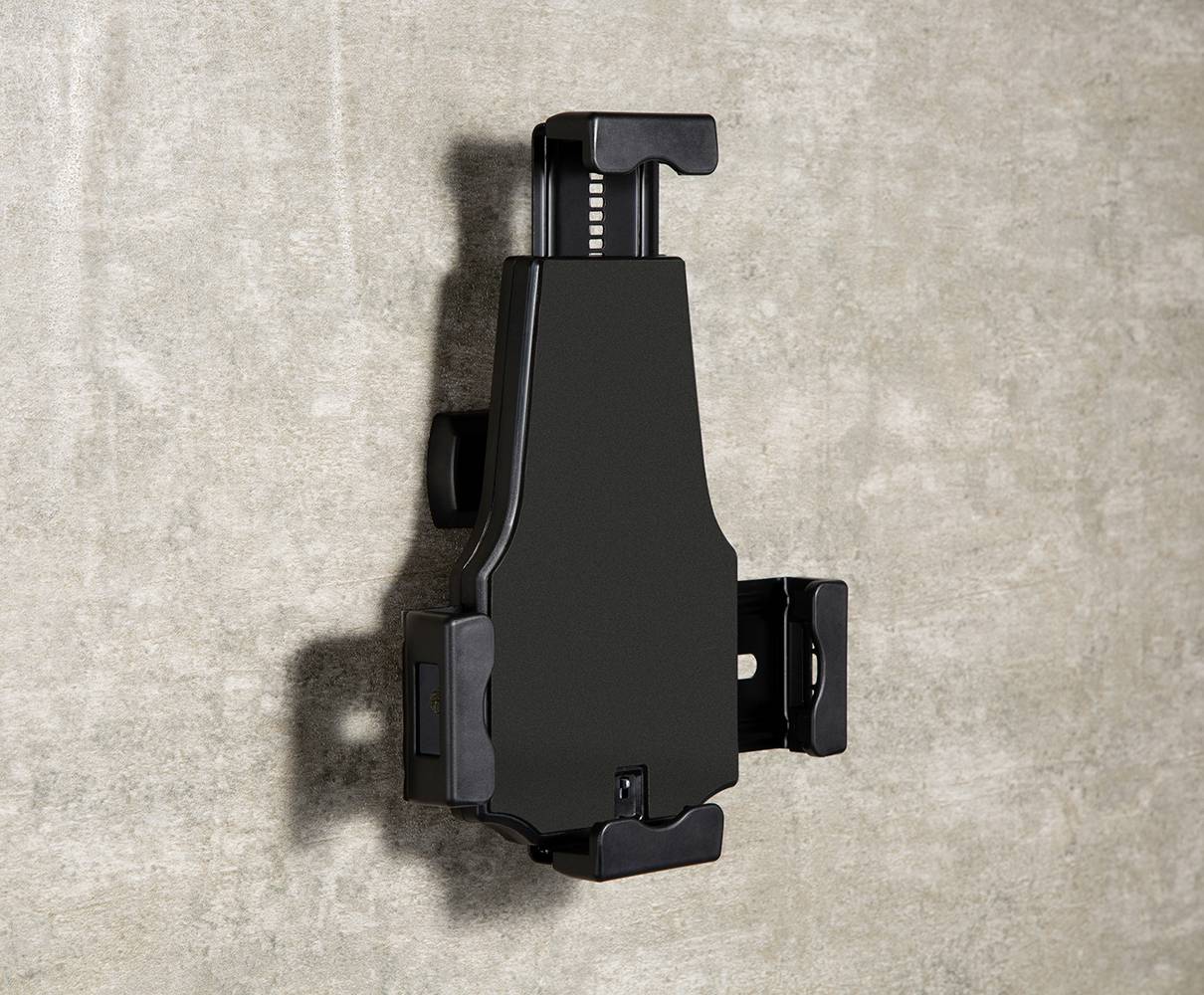 Fekete műanyag fali tartó, tabletekhez vagy okostelefonokhoz, betonfalra szerelve.