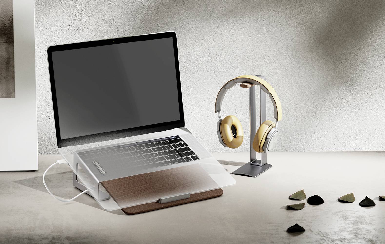 Egy laptop egy asztalon, laptoptartóval, egy fejhallgató-állvánnyal mellette. A háttérben szétszórva kisebb kiegészítők találhatók.