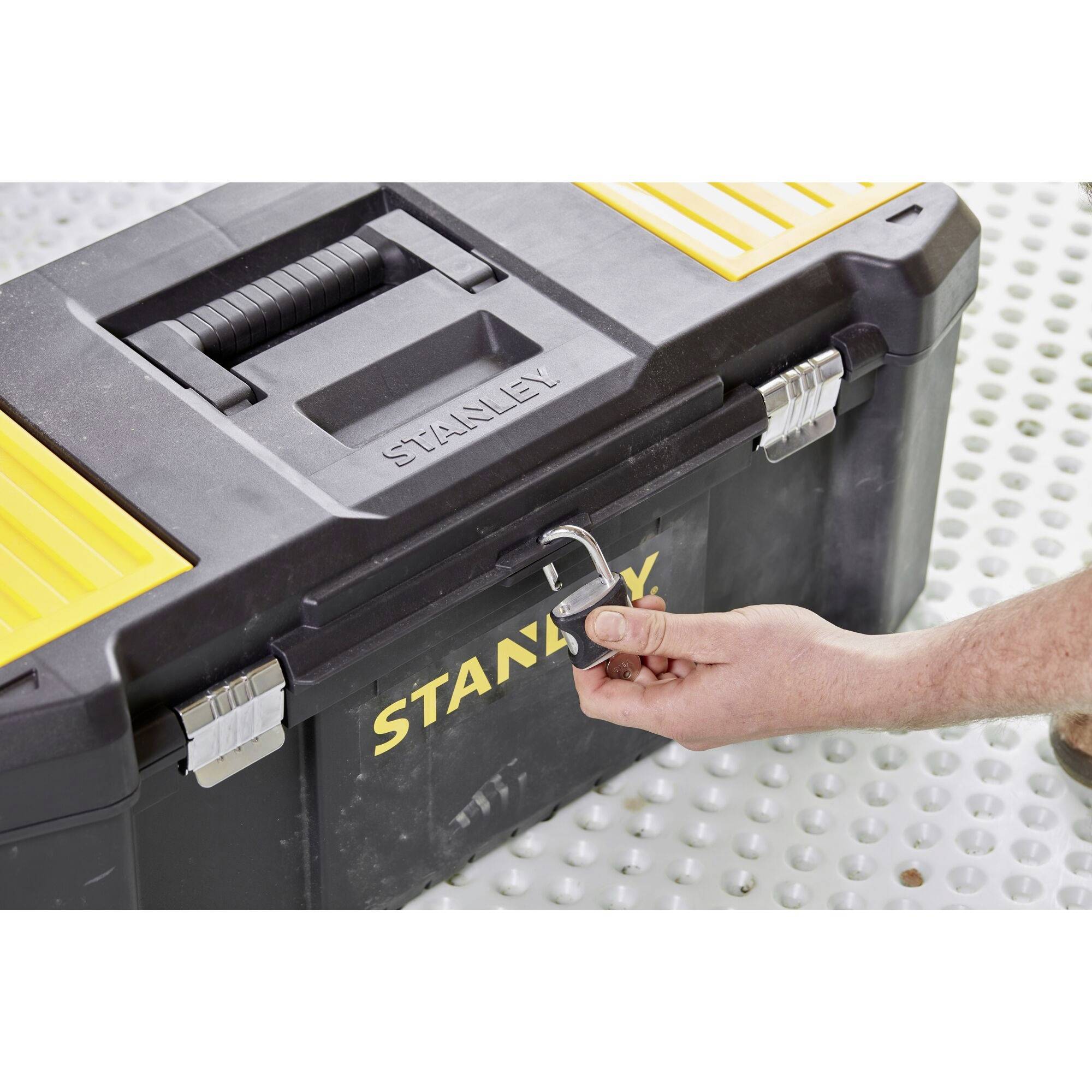 Egy ember lezár egy fekete szerszámosládát egy lakattal. A szerszámosláda sárga részletekkel rendelkezik és a STANLEY feliratot viseli.