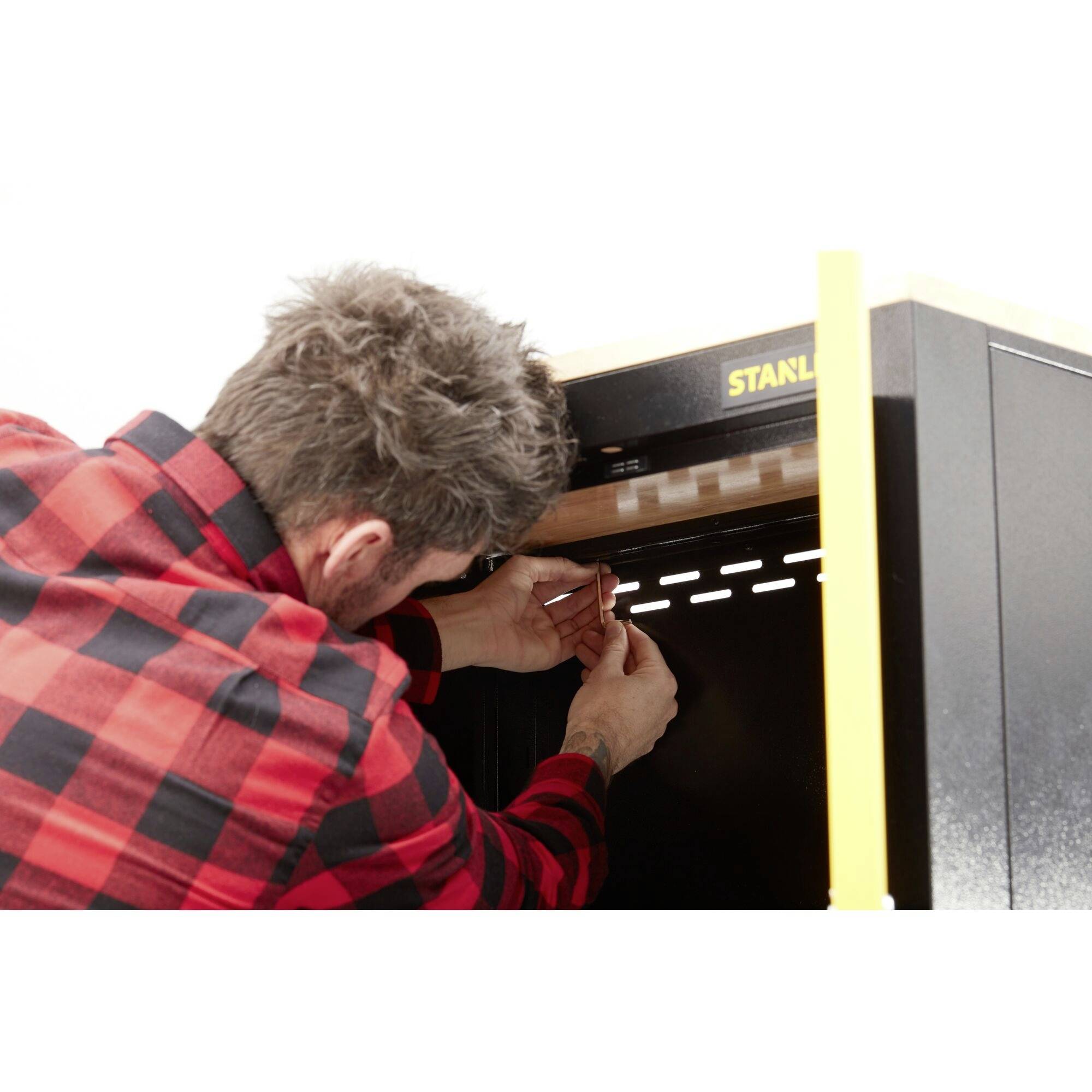 Egy kockás ingű személy koncentráltan dolgozik egy fekete fémszekrényen, miközben kisméretű szerszámokat használ valami beállításához.