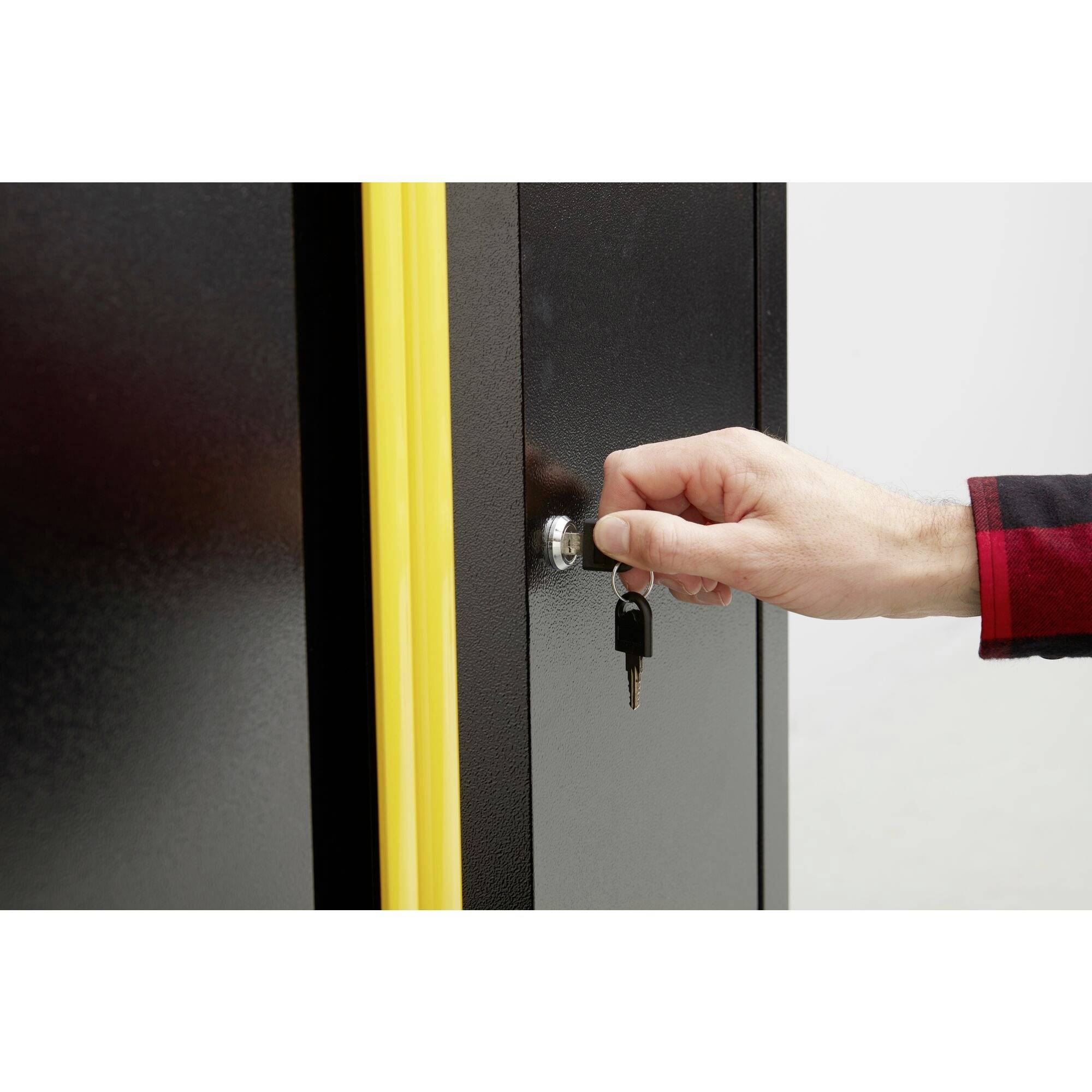 Egy kéz elfordít egy kulcsot egy fekete szekrény sárga szélű zárjában.