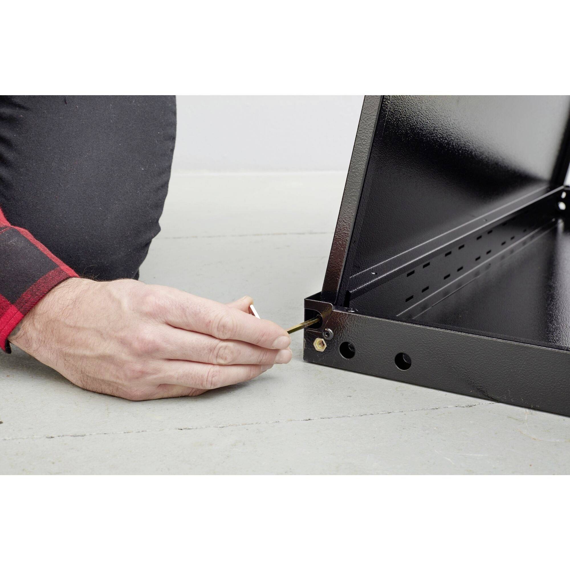 Egy személy egy bútordarabot szerel össze. Az egyik keze egy csavarkulcsot tart, a másik pedig alátámasztja a bútort. Kontextus: Kézművesség.