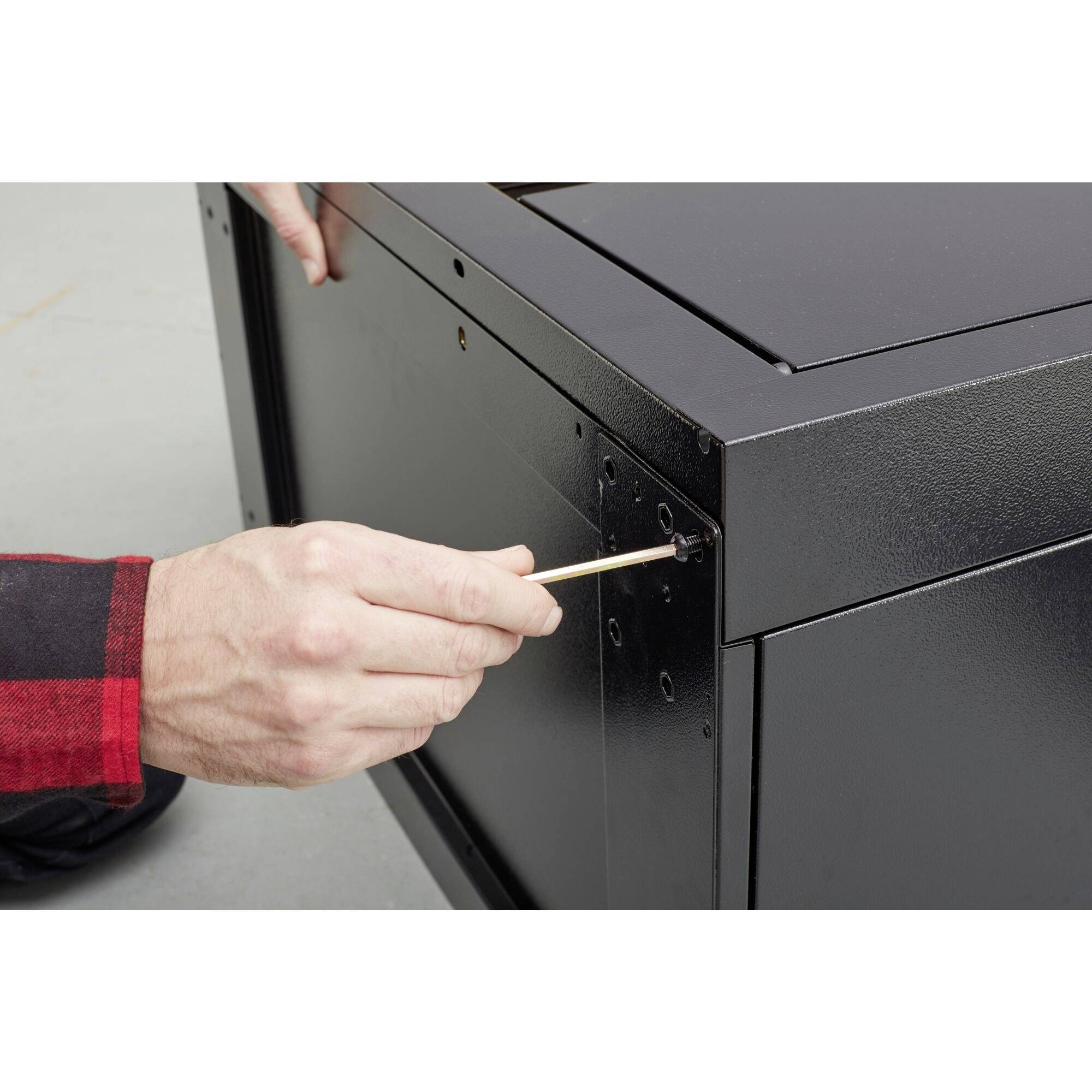 Egy piros-fekete ingbe öltözött kéz fogpiszkálót használ egy fekete búdarab csavarlyukainak kitisztítására.