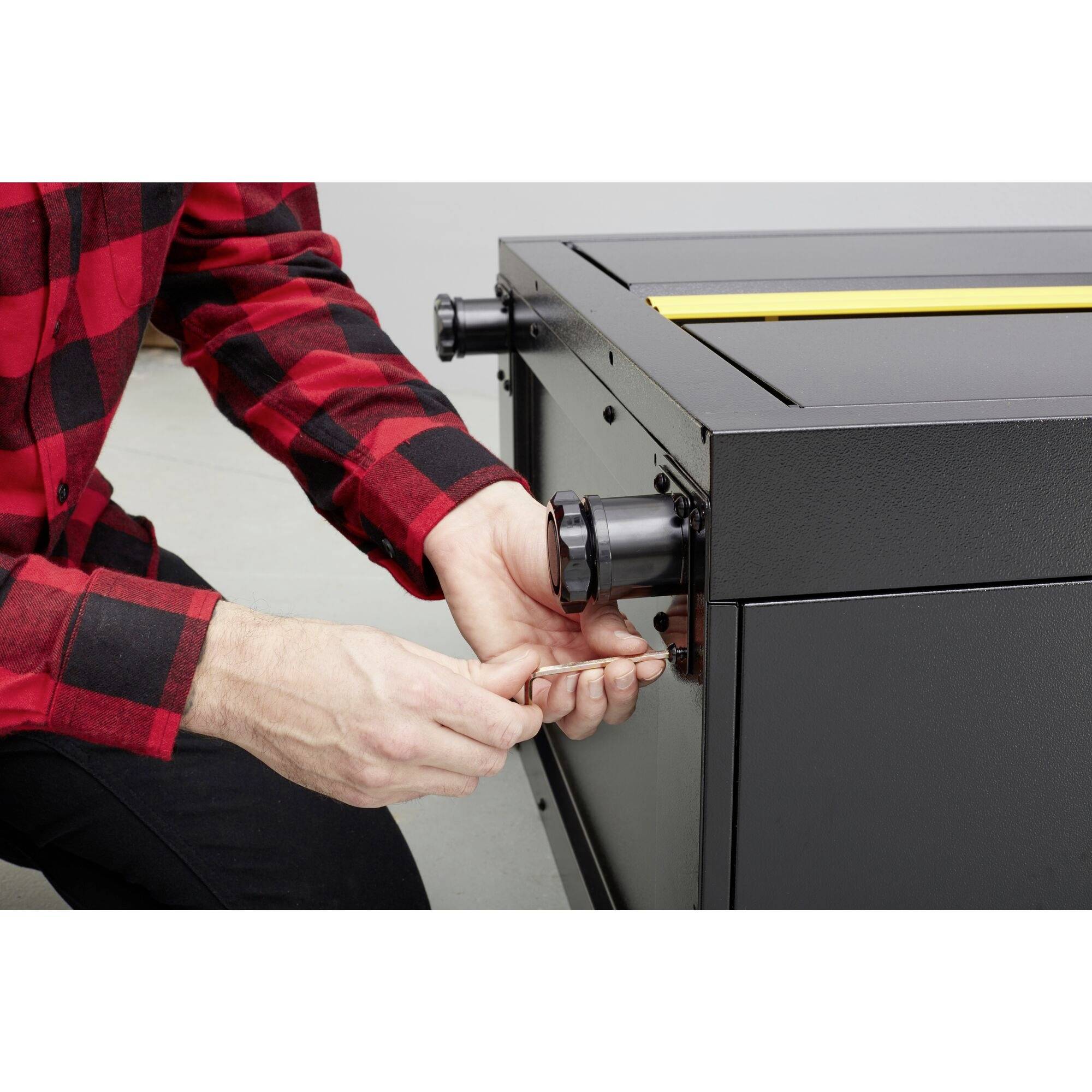 Egy piros-kockás ingű személy egy hatszögkulcsot használ egy fekete fémgép beállításához.