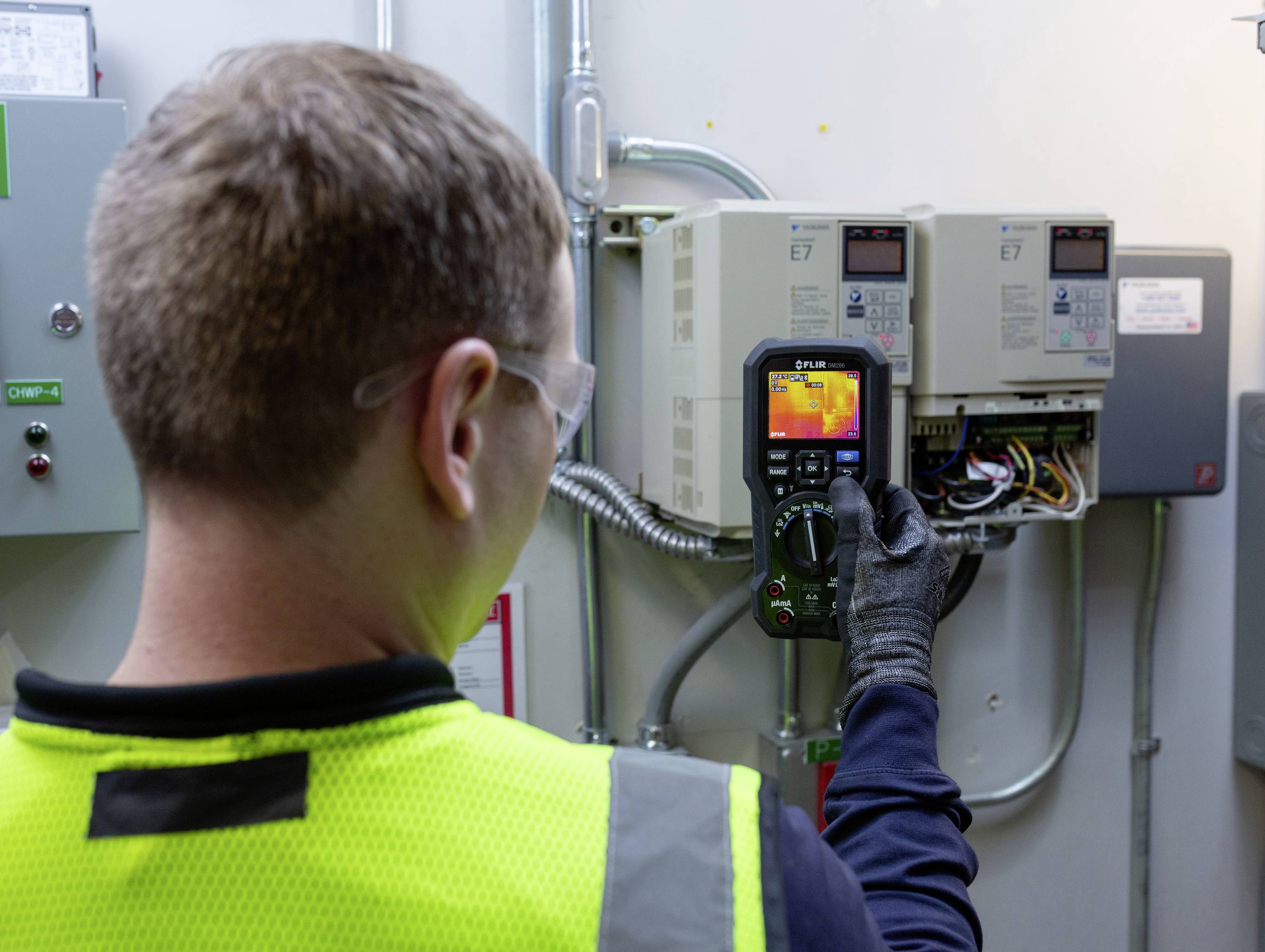 Egy technikus infravörös hőmérőt használ elektromos vezérlőegységek ellenőrzéséhez egy karbantartó helyiségben.