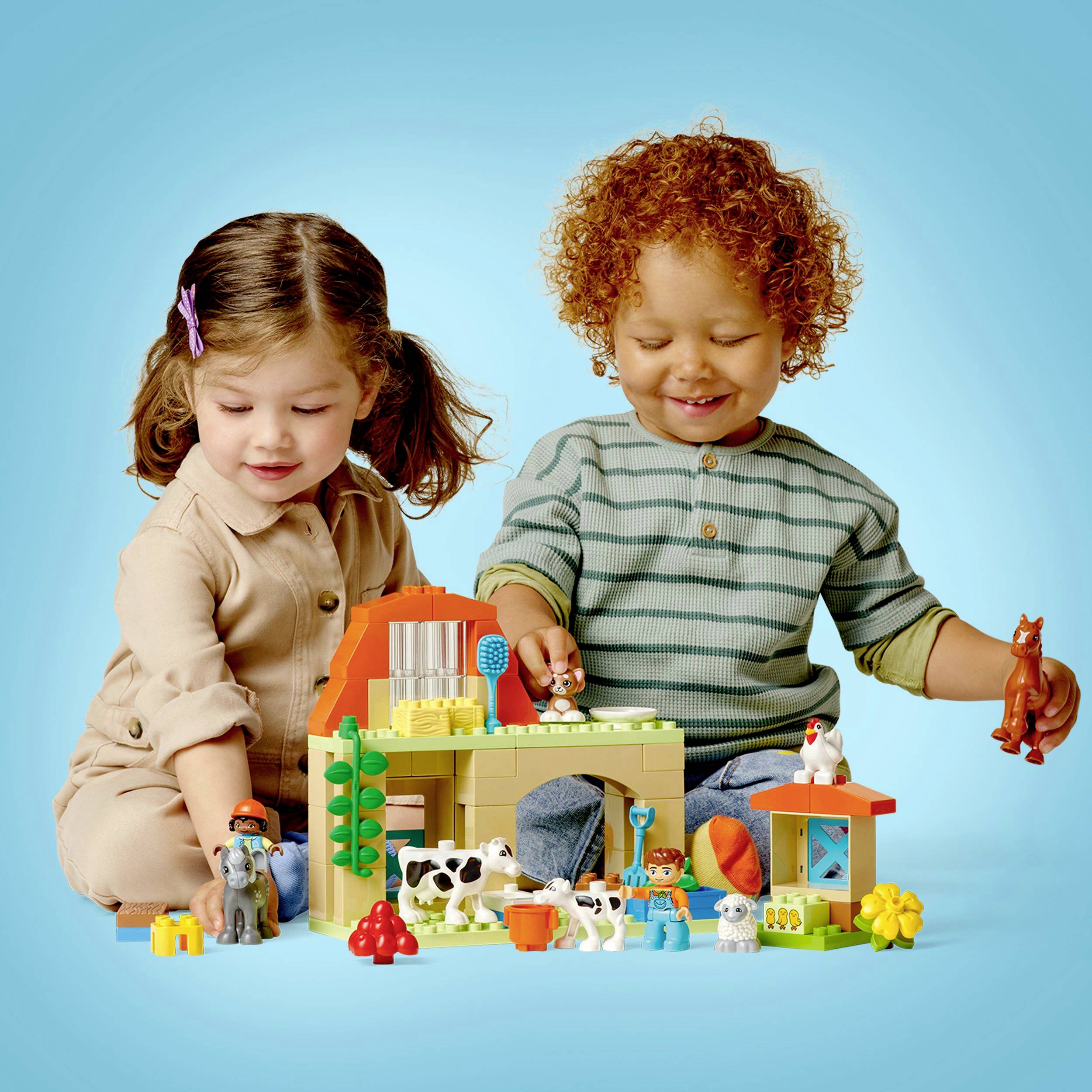 Két gyerek egy fa farm-játékszett segítségével játszik. Az állatok és a fák szét vannak szórva az asztalon.