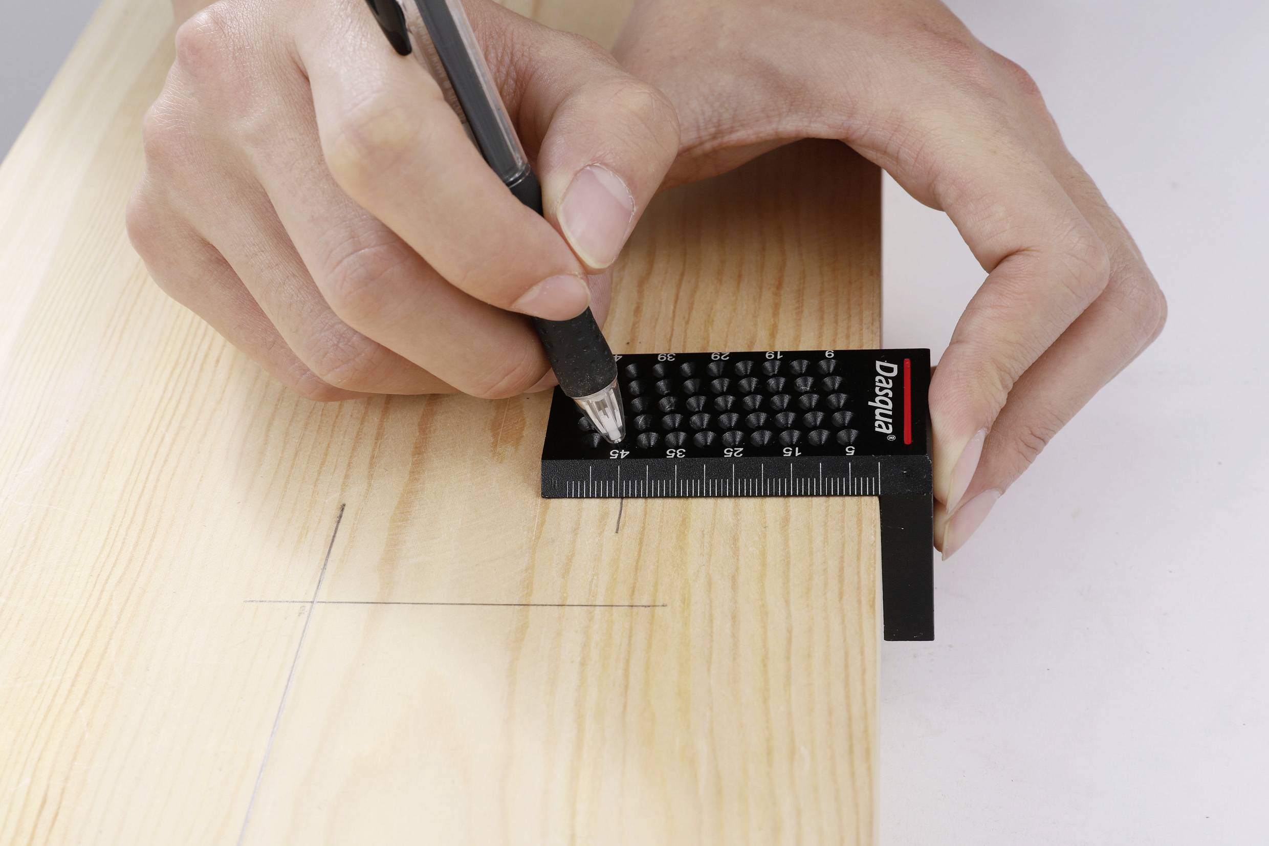 Egy kéz egy tollat tart, és egy fekete vonalzóval pontosan egy vonalat húz egy fadeszkán mérési célból.