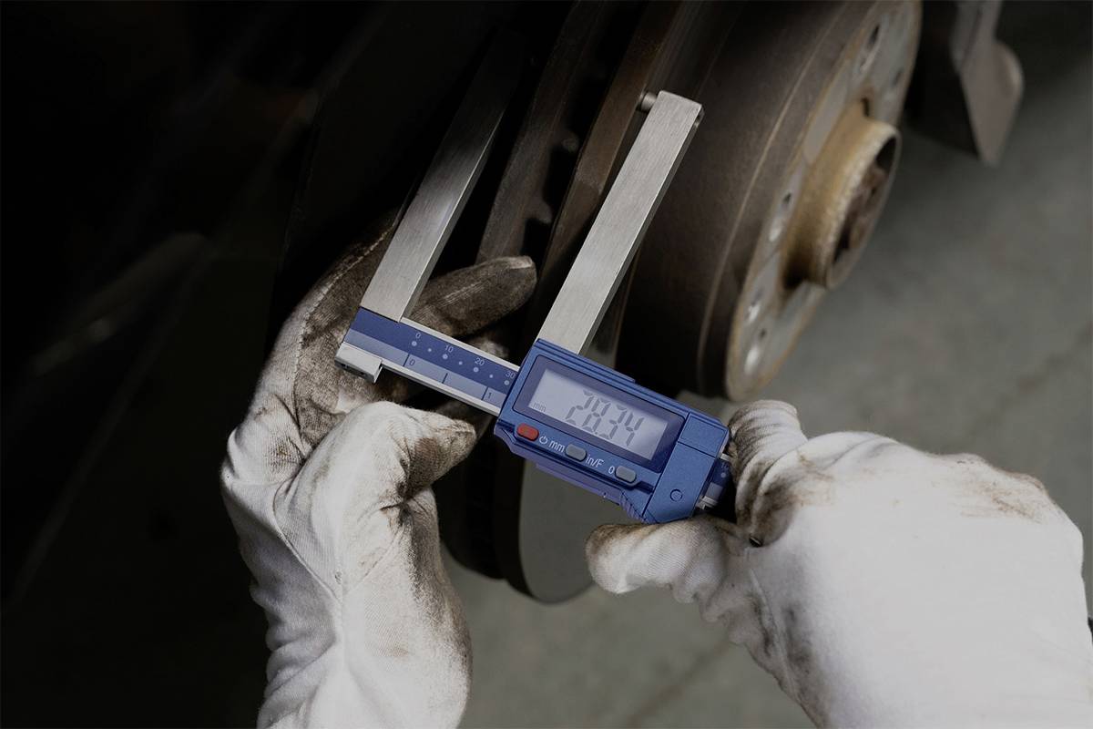 Két gumikesztyűs kéz digitális tolómérővel méri egy fékbetét átmérőjét.