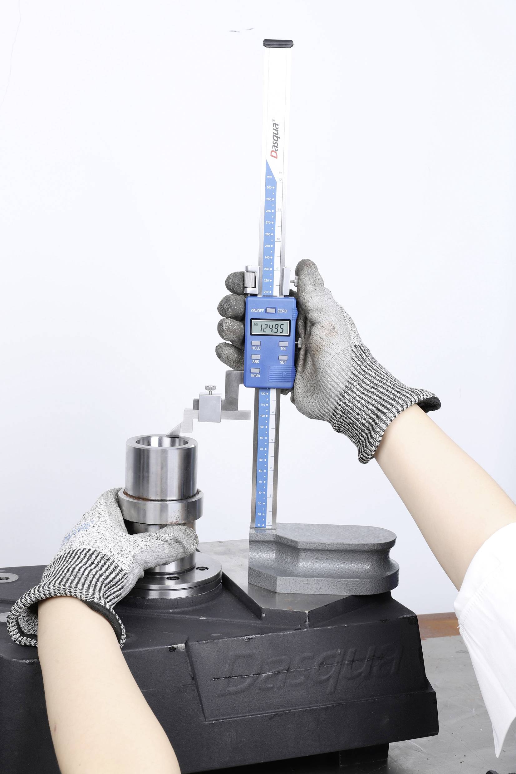 Egy személy magassági mérőműszerrel mér egy hengeres alkatrészen. A digitális kijelző '12,985'-et mutat.