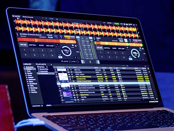 Egy laptop képernyőjén DJ-szoftver látható több zenei sávval, lejátszási listákkal és hullámforma-vizualizációkkal.